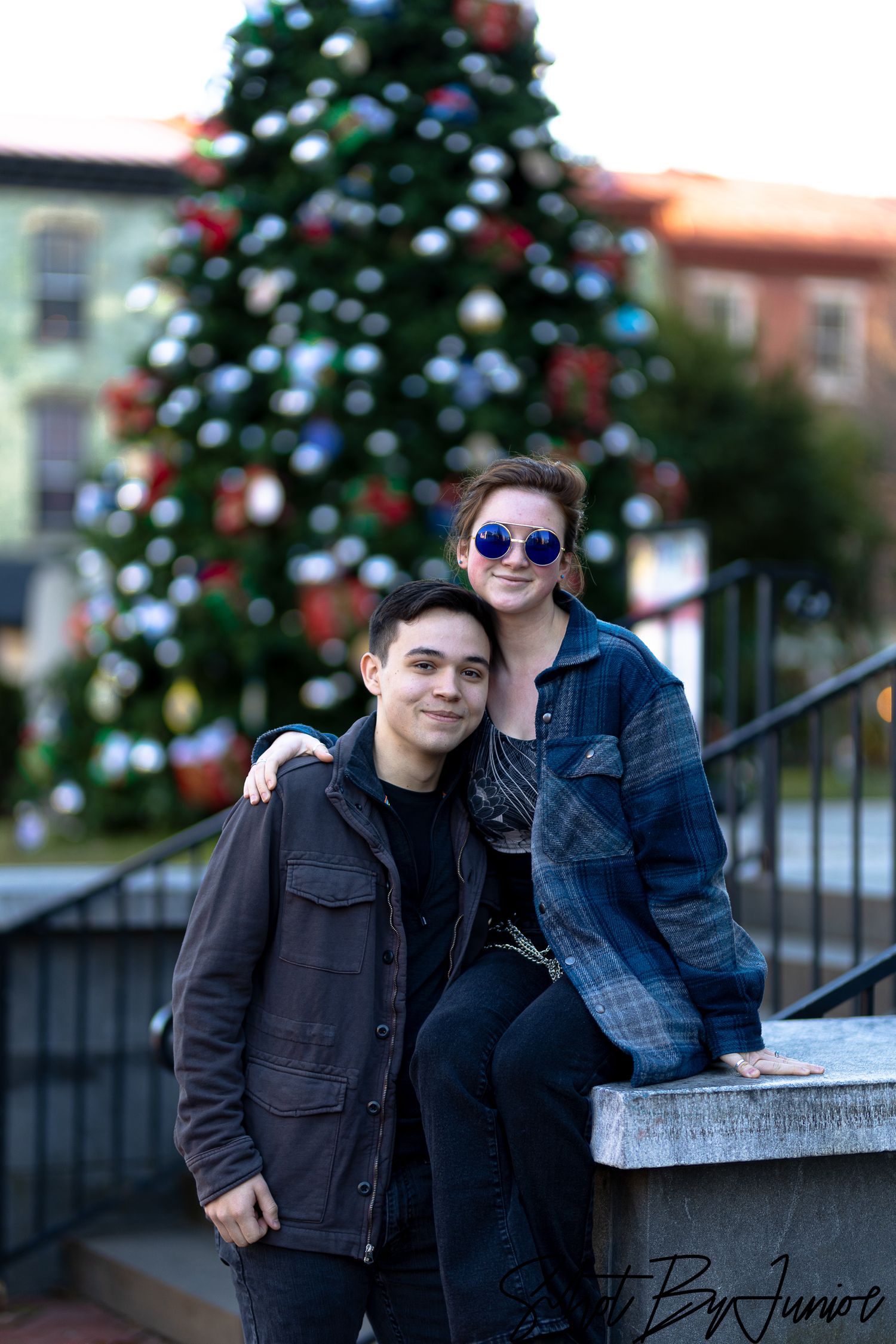 Couple posing in winter jackets in front of decorated Christmas tree.