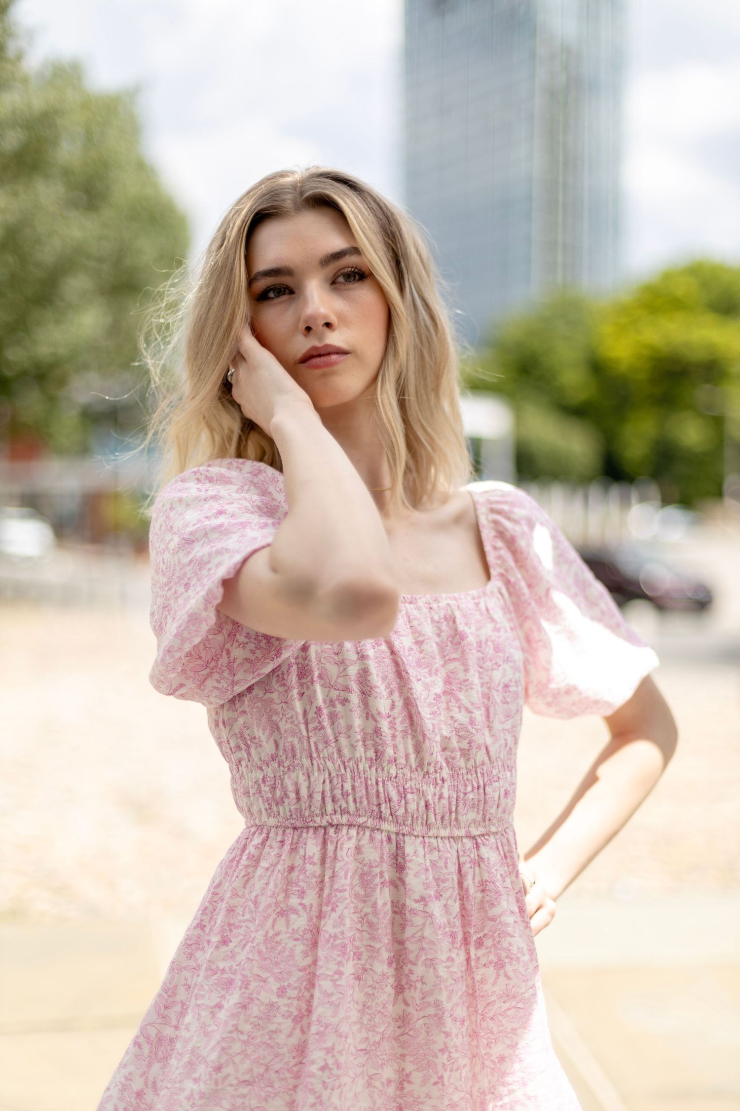 Fashion portrait of woman in pink dress against urban background with skyscraper.