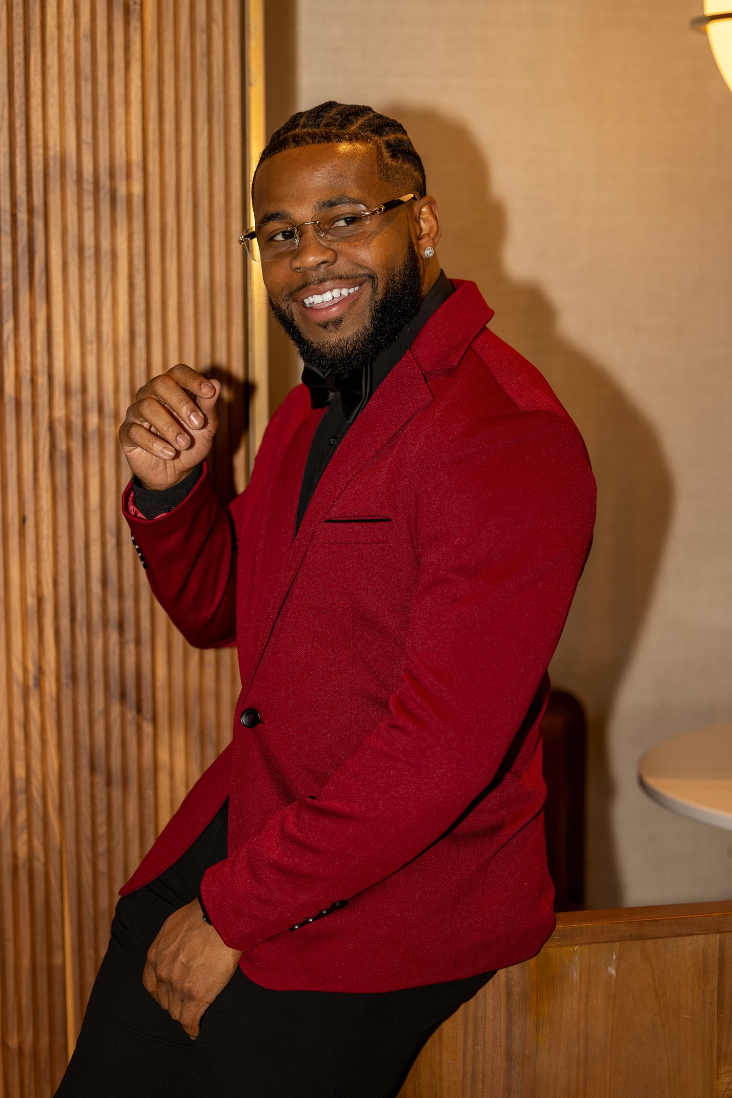 Man in red blazer and black bow tie poses against wooden paneled wall.