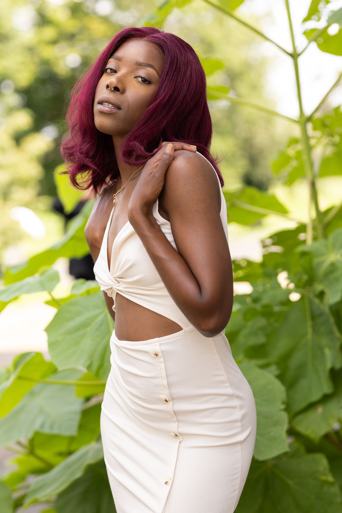 Artistic portrait in cream colored outfit against lush green garden backdrop.