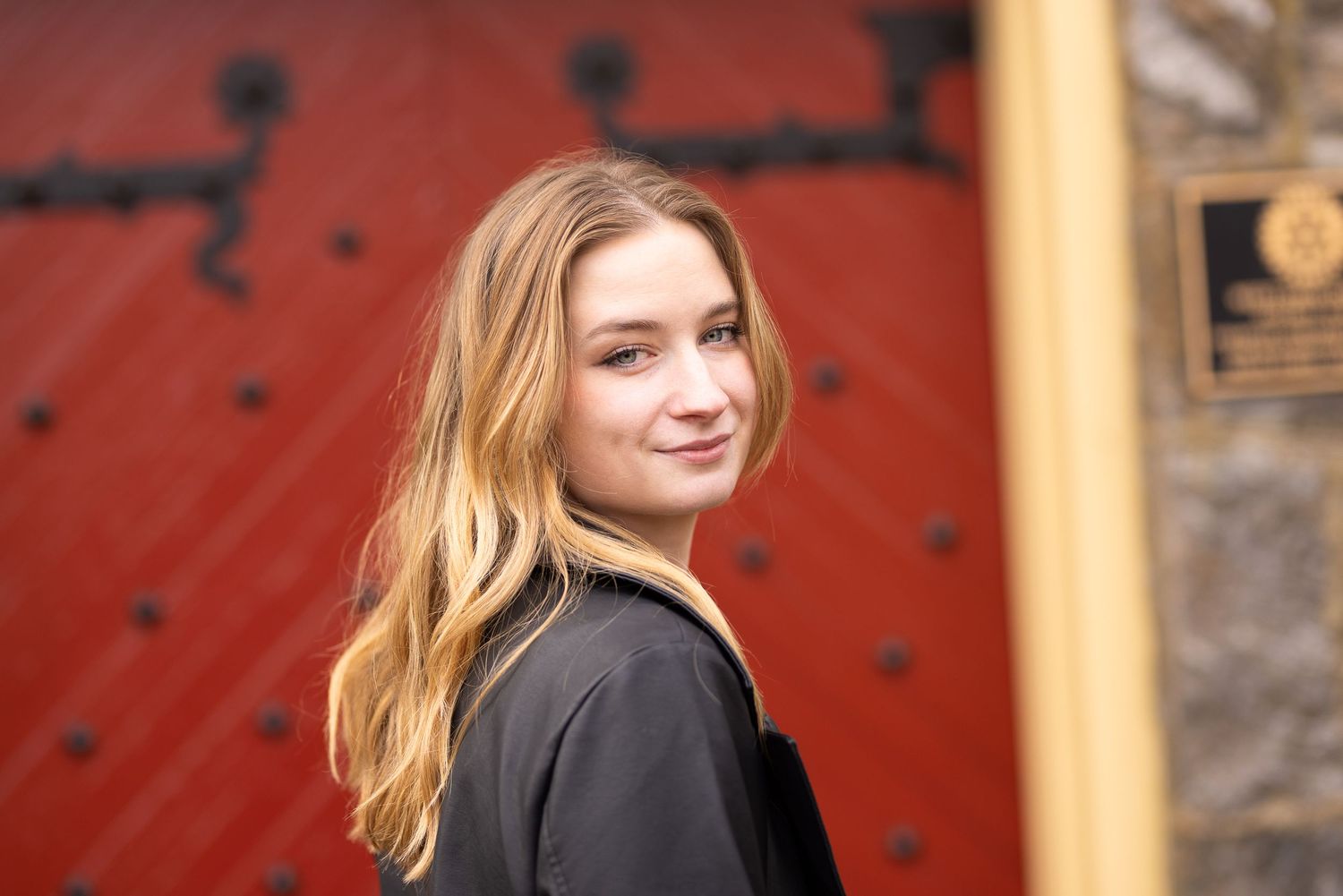 Portrait of person with long hair wearing black jacket against red door background.