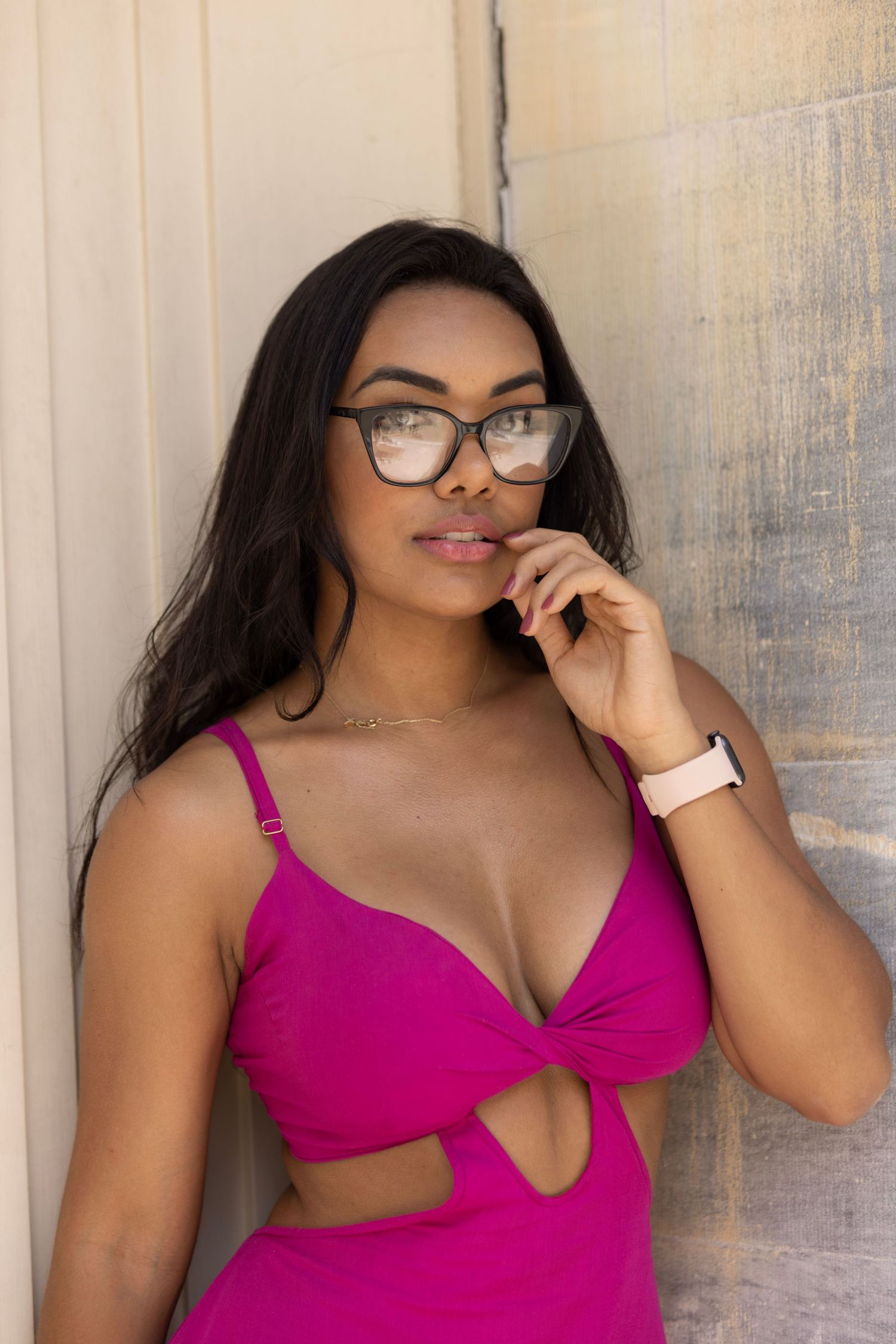 Fashion model in magenta cutout dress wearing stylish glasses poses against light wall.