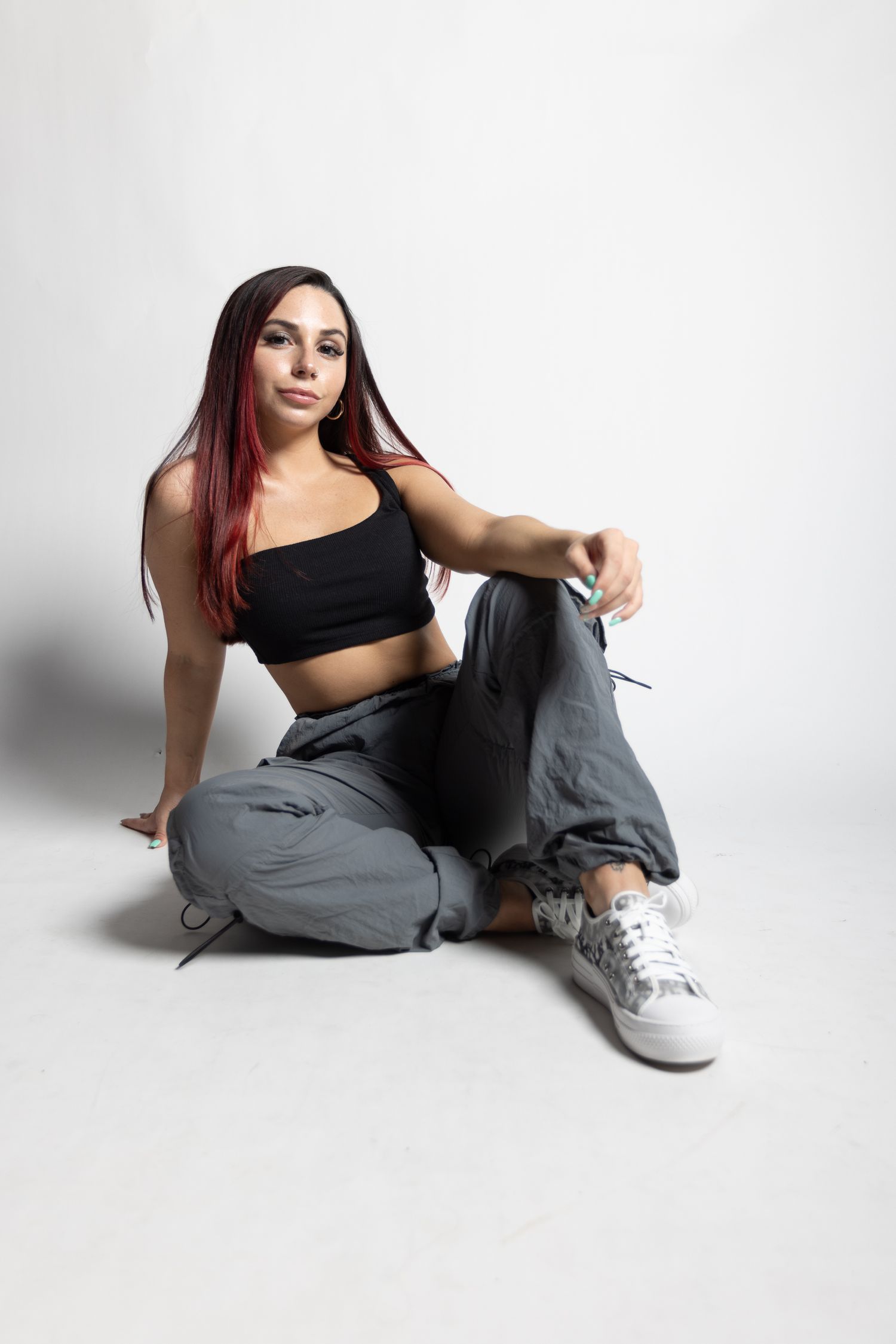 Woman in athletic wear sits casually on white studio floor.