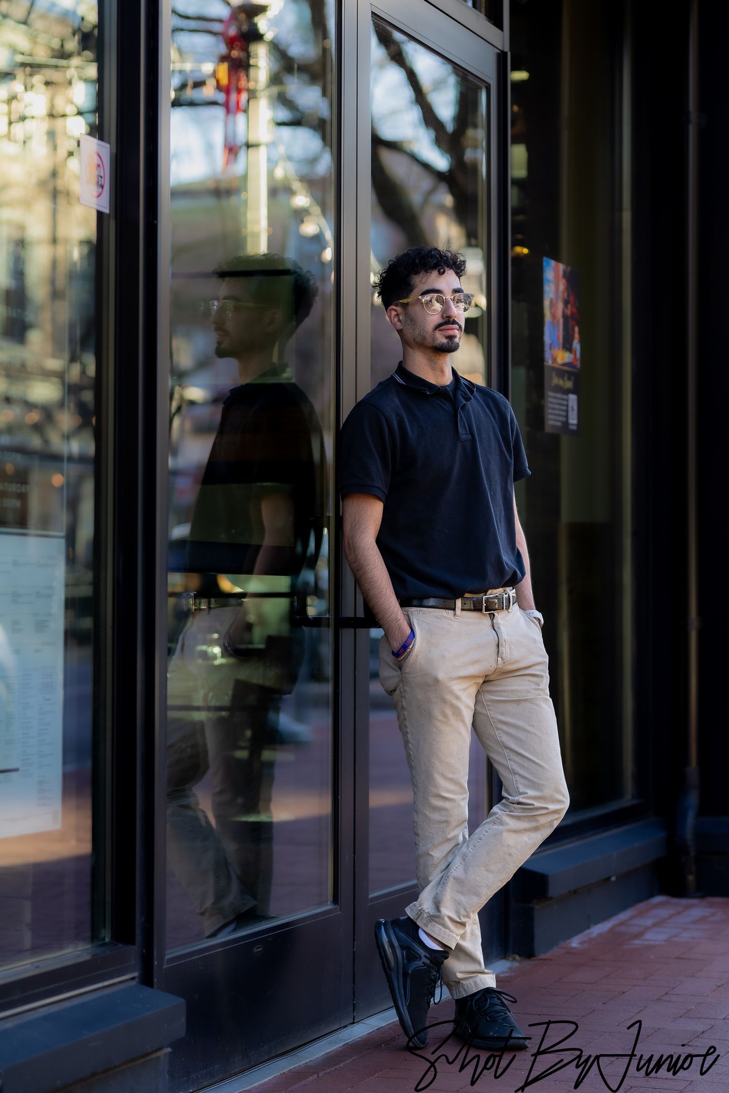 Portrait of person leaning against storefront window in casual attire.
