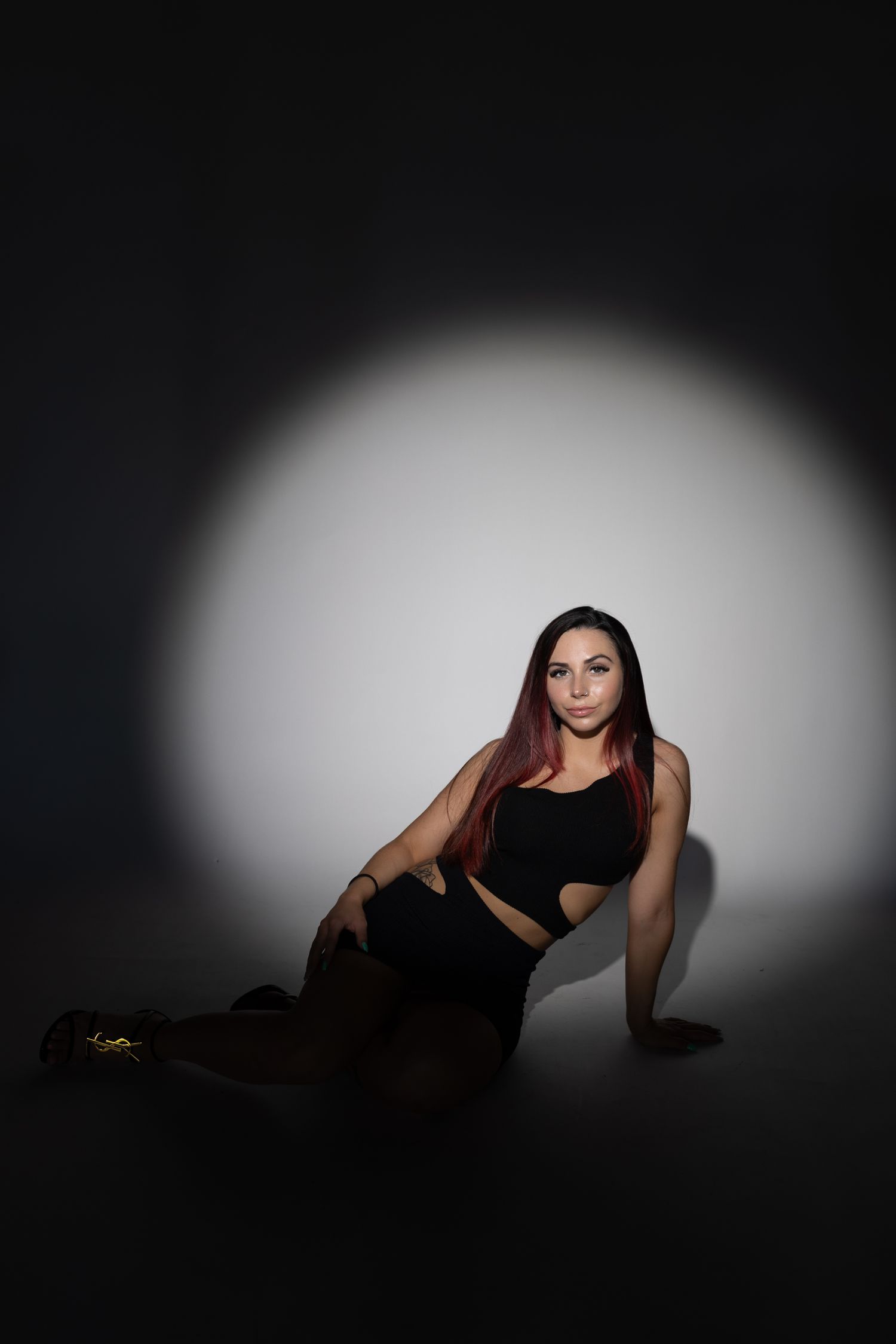 Studio portrait with dramatic spotlight of woman in black outfit against dark background.
