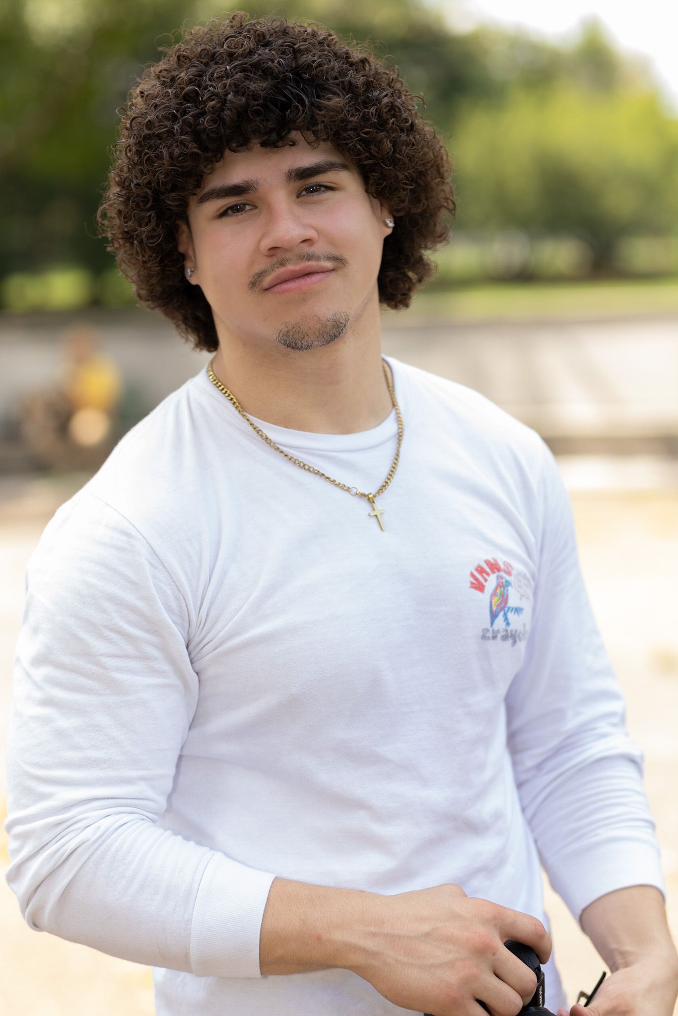 Portrait of person in white long sleeve shirt wearing silver necklace outdoors.