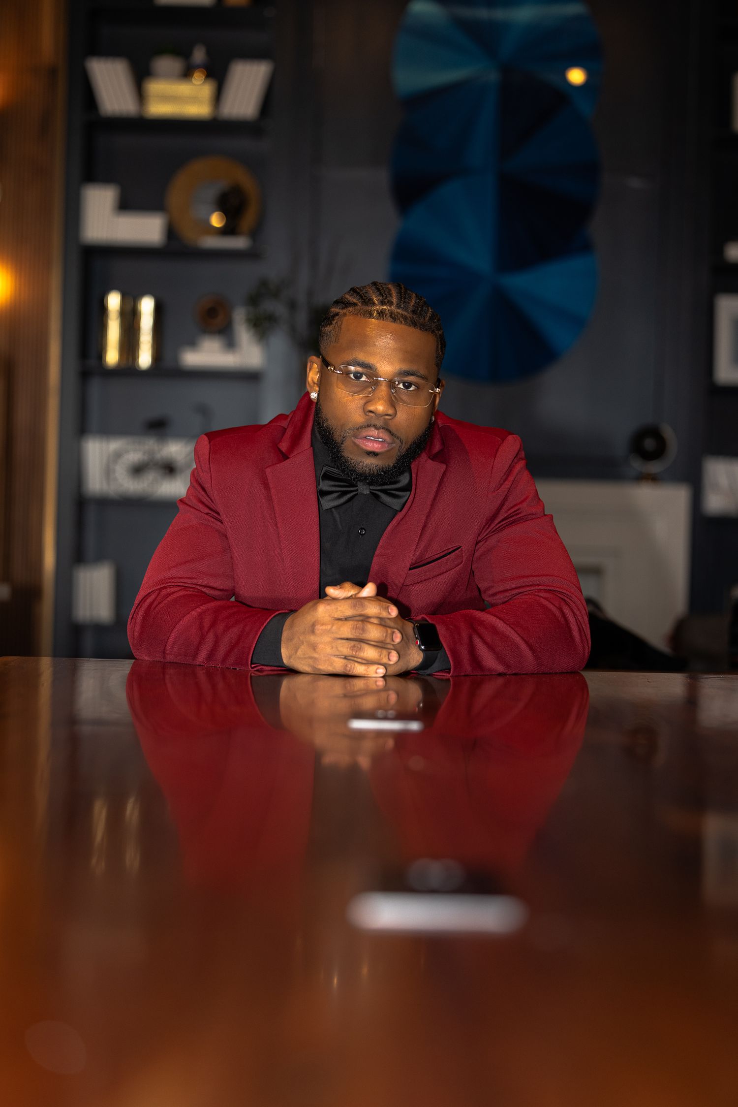 Professional seated at wooden table wearing red blazer in modern office setting.