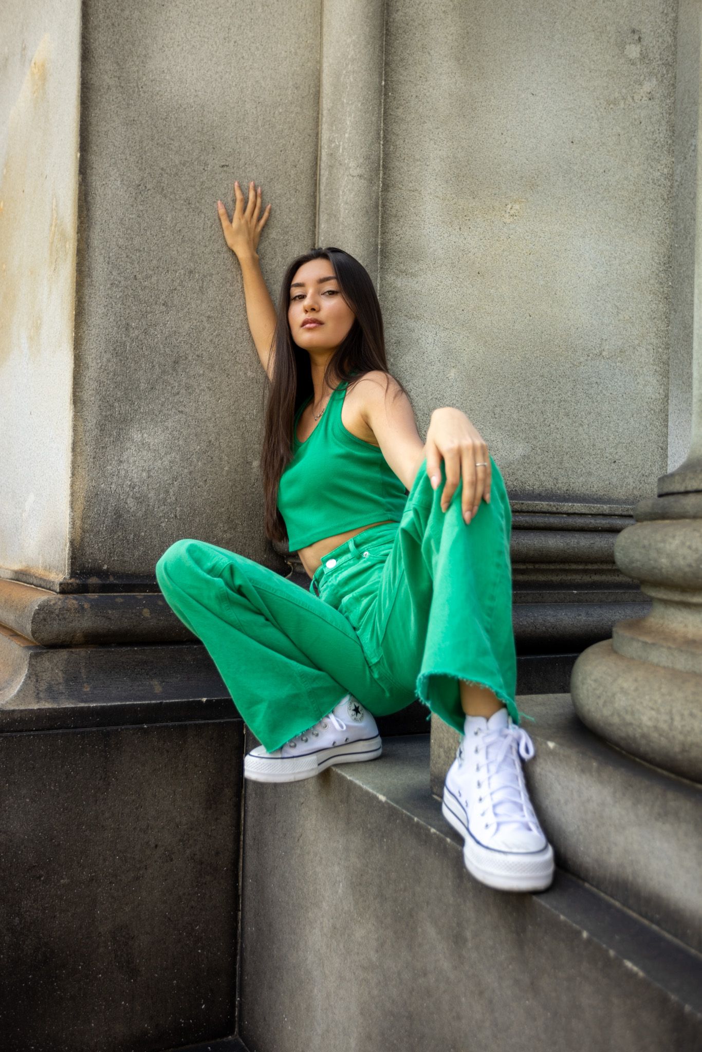 Athletic pose in bright green matching set and white sneakers on concrete steps.