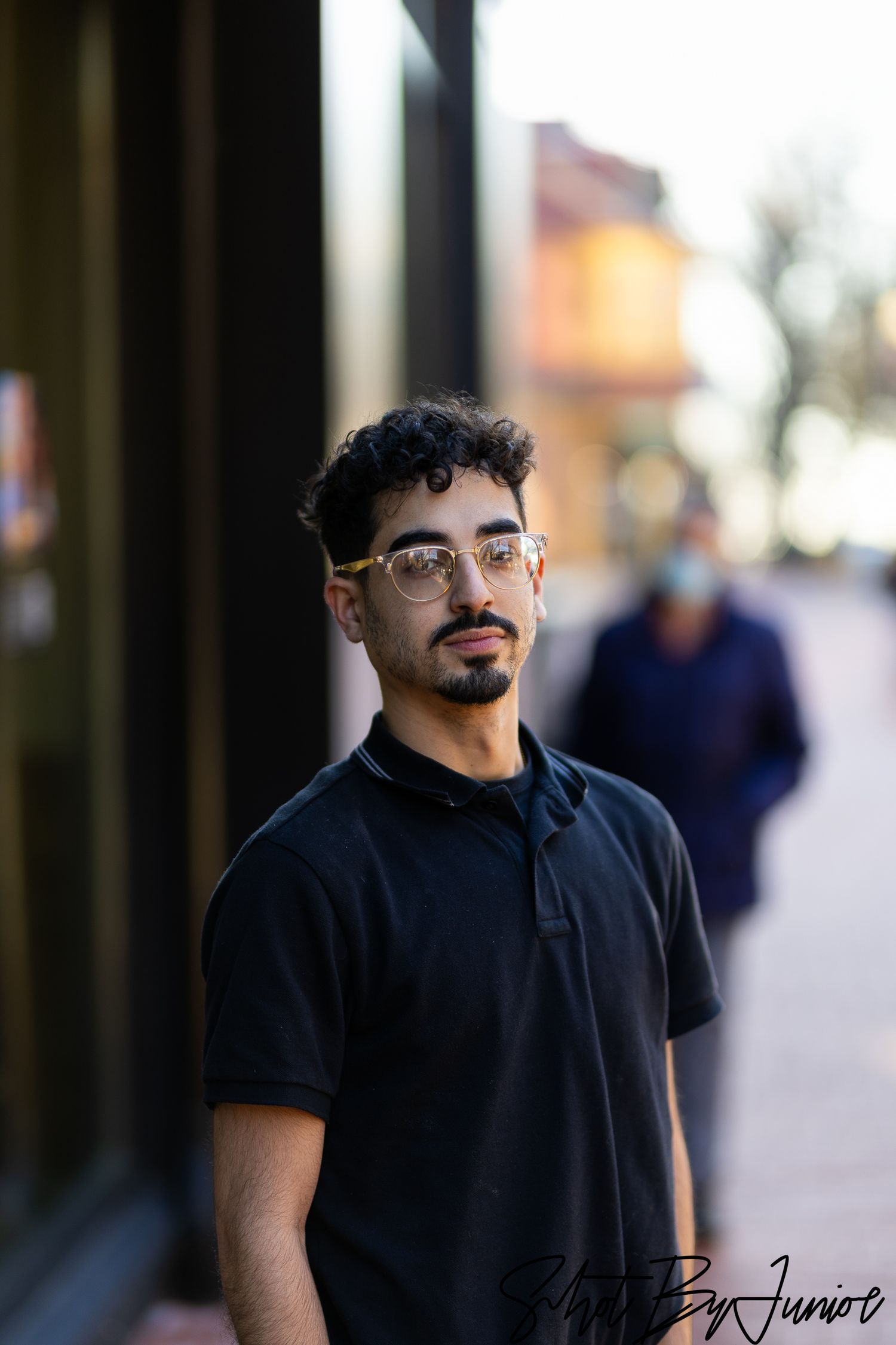 Street style portrait of person in black polo against urban backdrop.