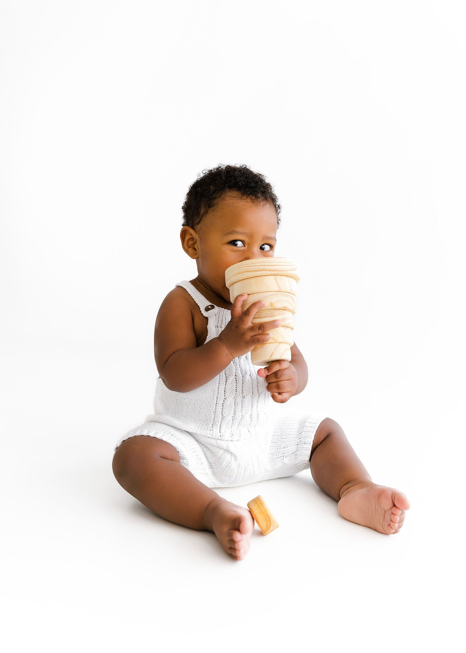 Baby in white romper drinking from cone-shaped cup against white background.