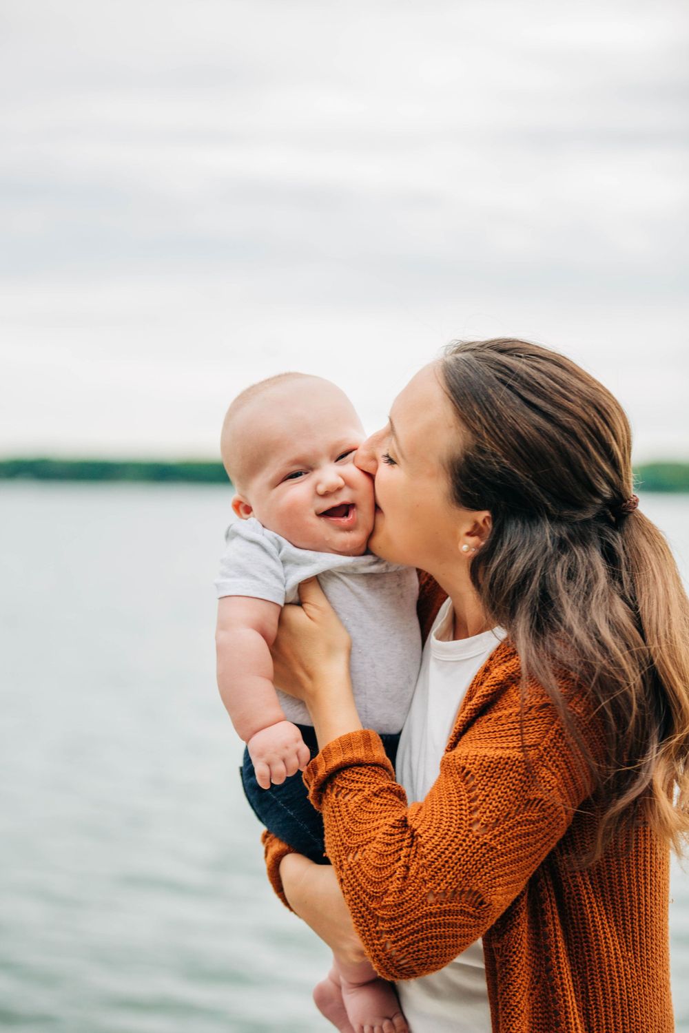 A mom kisses her chubby baby boy near the lake by Traverse City family photographer Grace Hudson