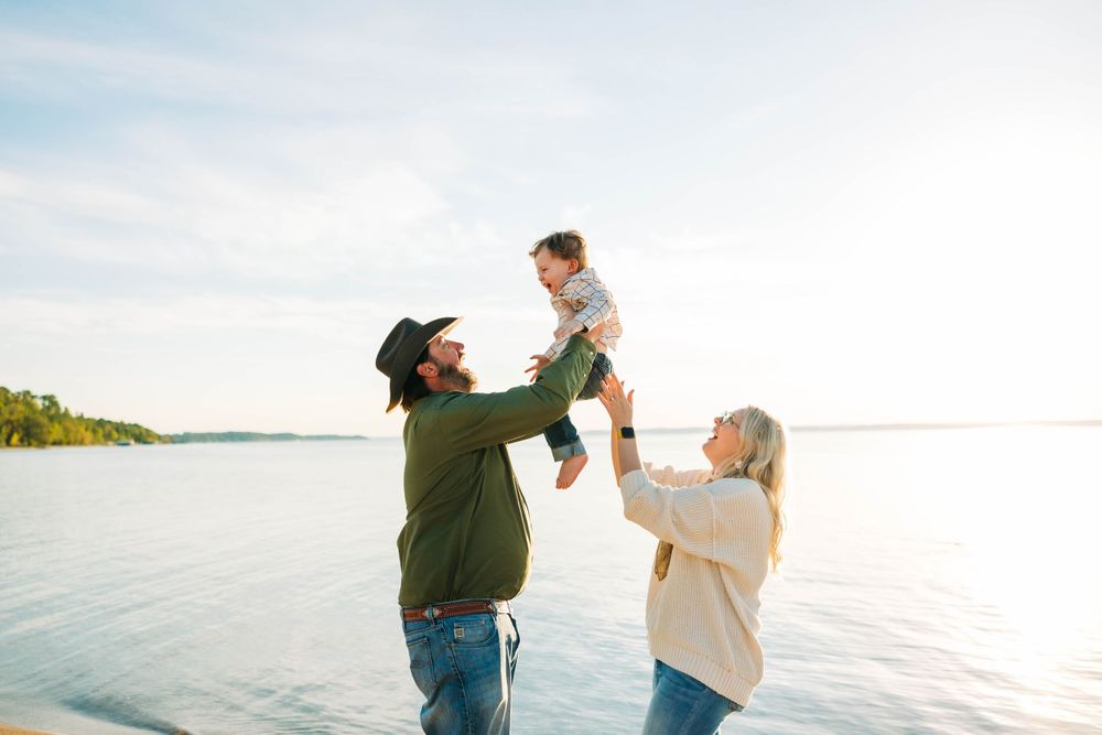A family holding their son up a the beach at sunset by Traverse City family photographer Grace Hudson