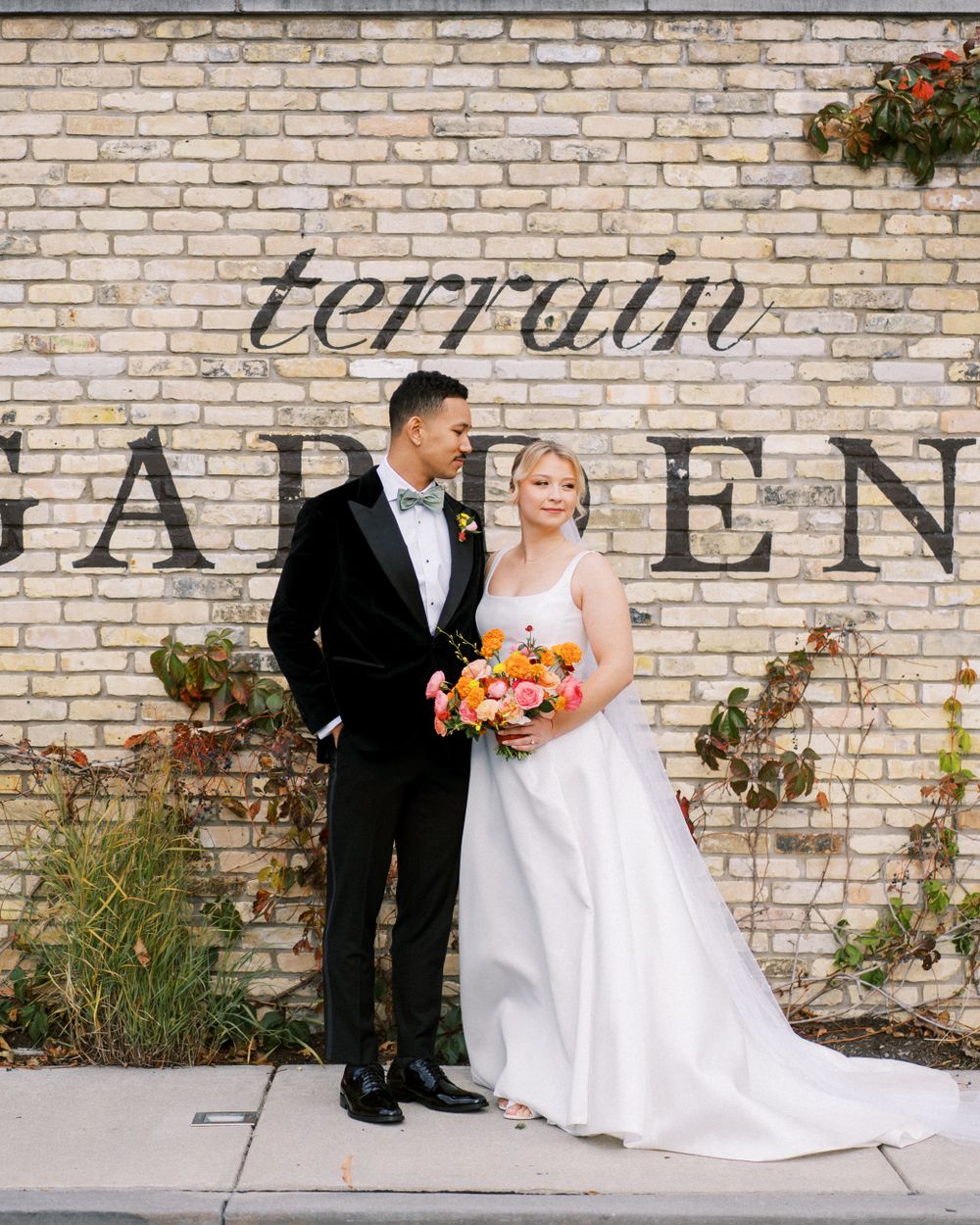Wedding couple poses in front of brick wall with 'terrain garden' signage.