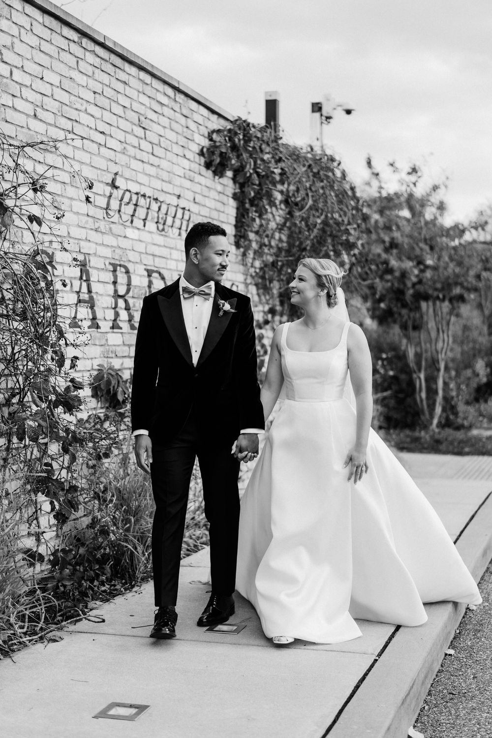 Wedding couple walking along brick wall with 'terrain' signage in black and white.
