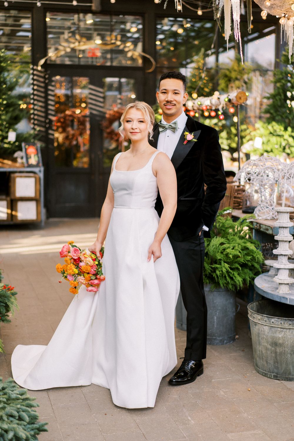 A wedding couple poses in a lush garden venue with string lights and autumn florals.
