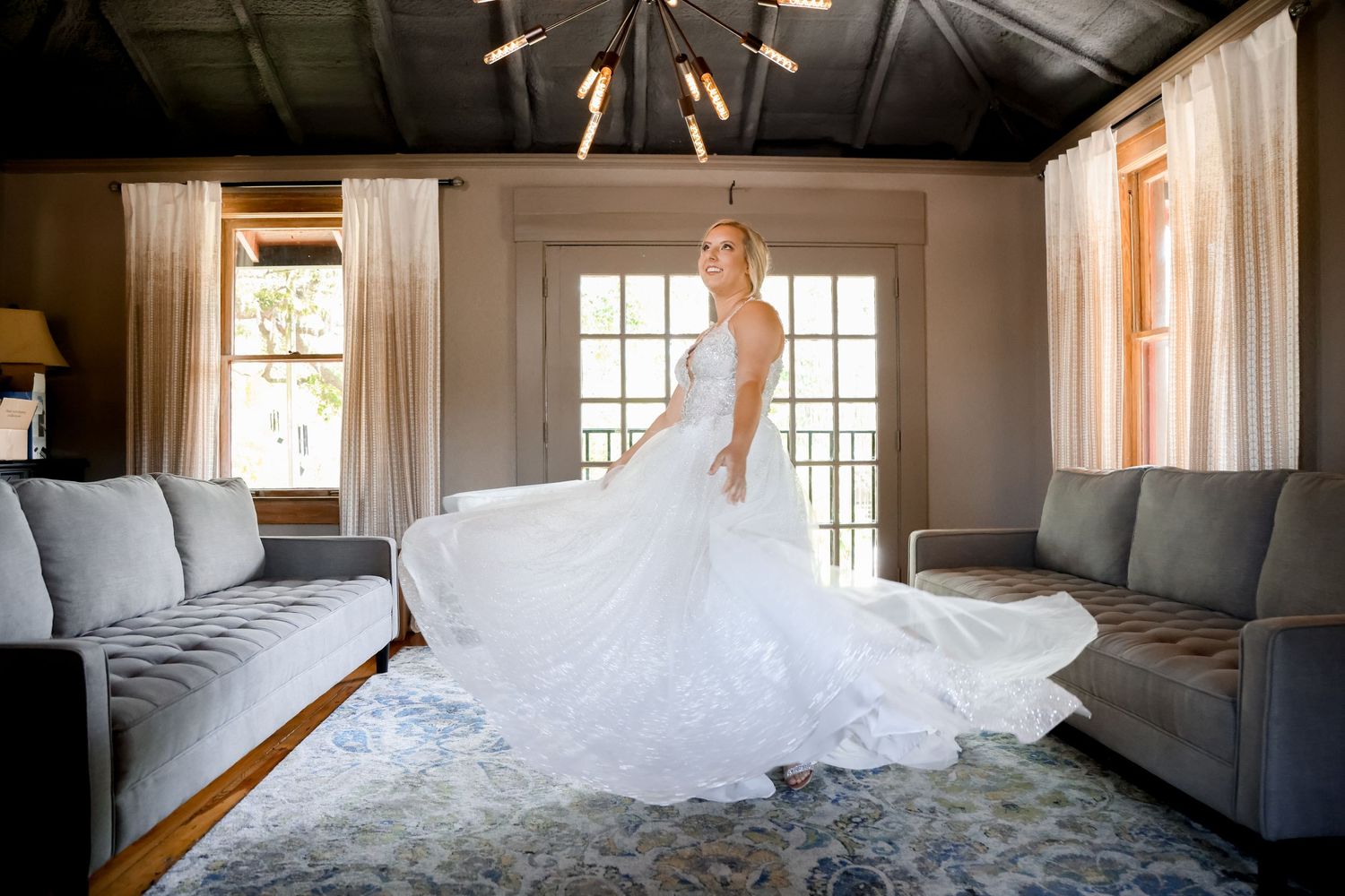 Wedding dress with long train displayed elegantly in sunlit room with gray couches.