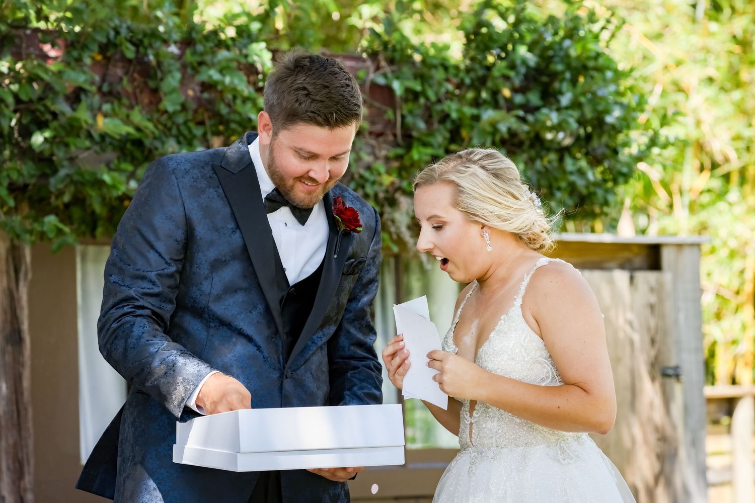 Wedding couple sharing an excited moment while looking at a gift box during their outdoor celebration.