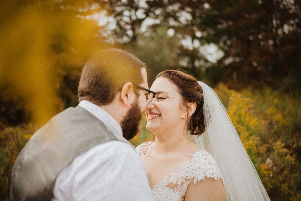 Candid outdoor wedding portrait capturing a romantic moment through golden autumn foliage.
