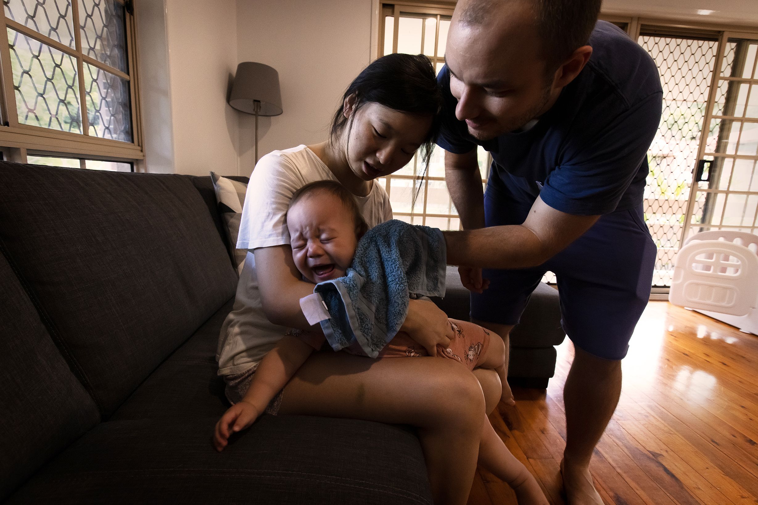 A father and mother hold their crying toddler as they try to wipe his face with a small towel.