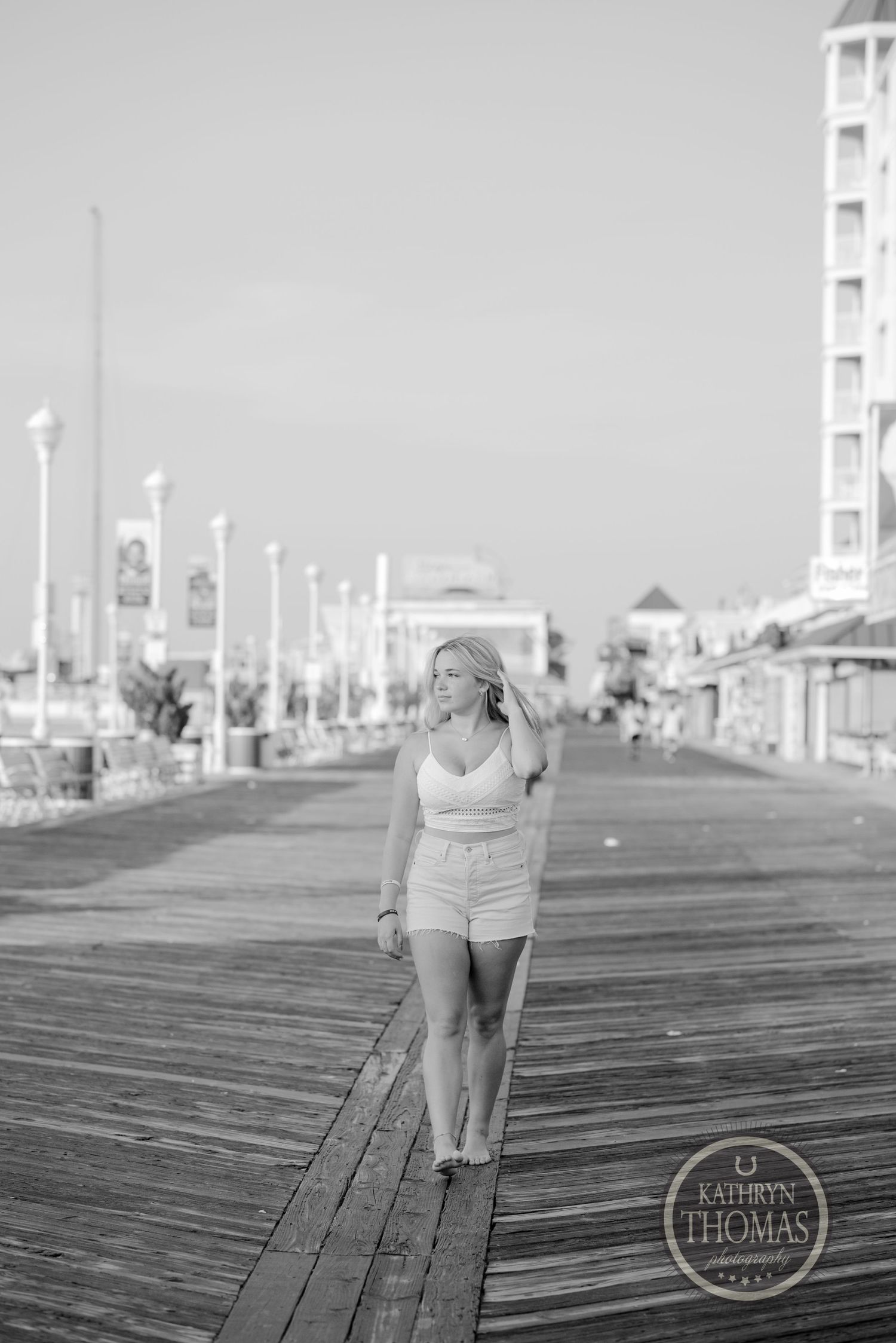 Black and white photograph of a person walking along a wooden boardwalk with lampposts.