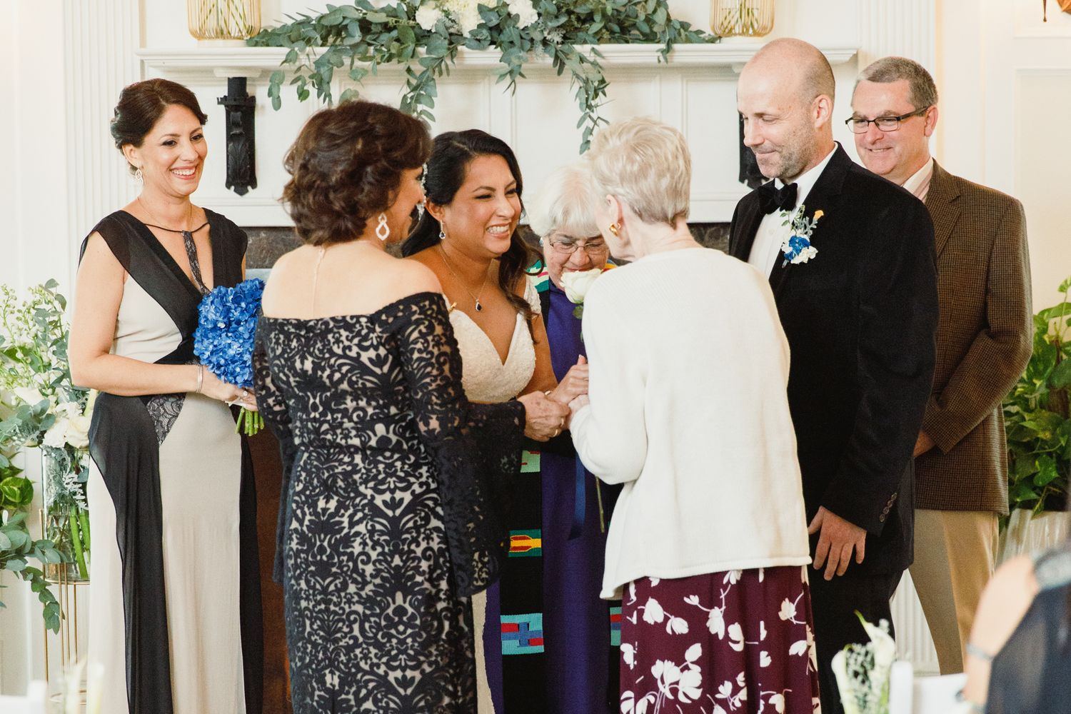 Wedding party members gather during ceremony in an elegant room with floral decorations.