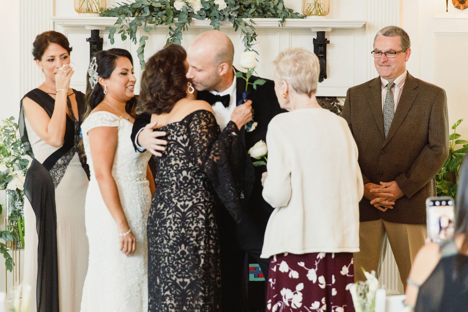 Wedding guests mingle in an elegant room decorated with greenery and white decor.