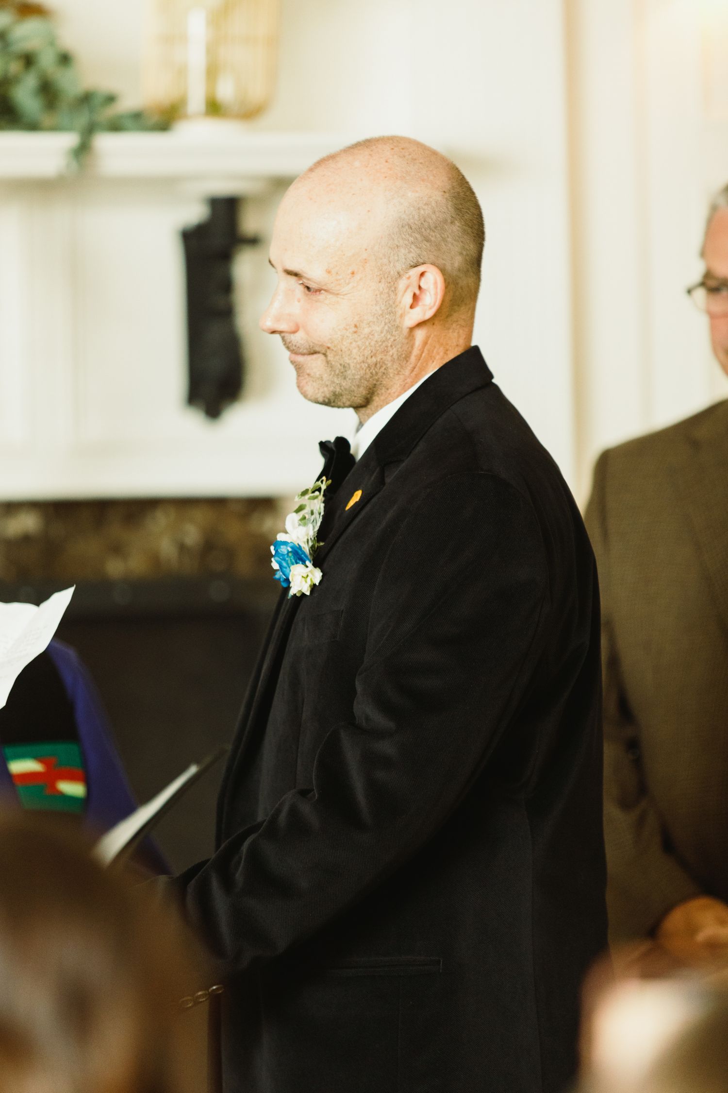 Person in black formal attire stands during wedding ceremony in elegant indoor setting.
