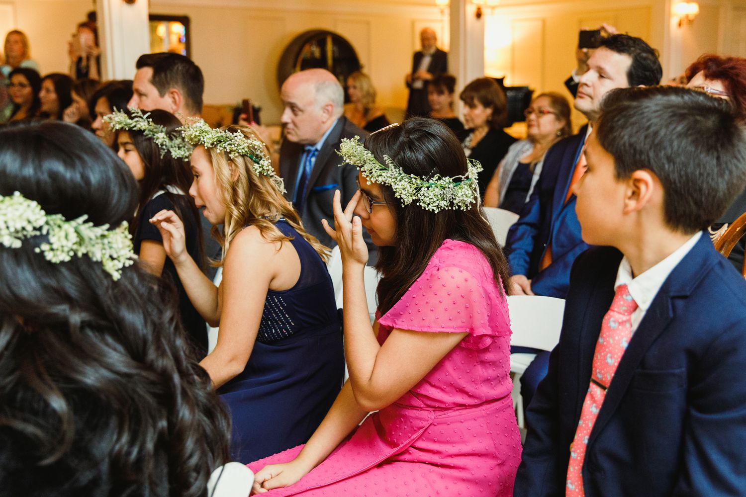 Wedding guests watch intently during an indoor ceremony with bright lighting.