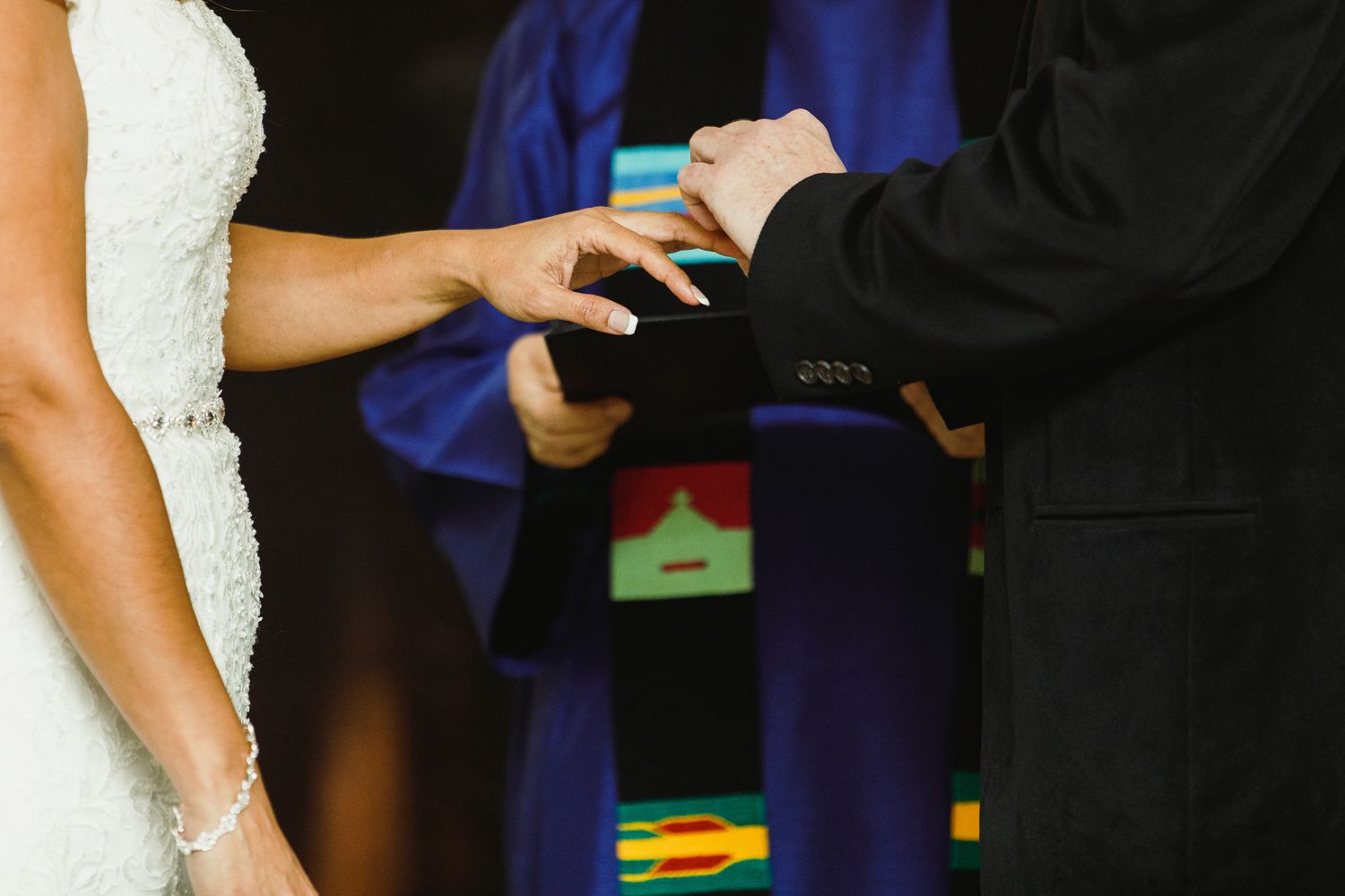 Close-up view of wedding ceremony participants in formal attire during an exchange.