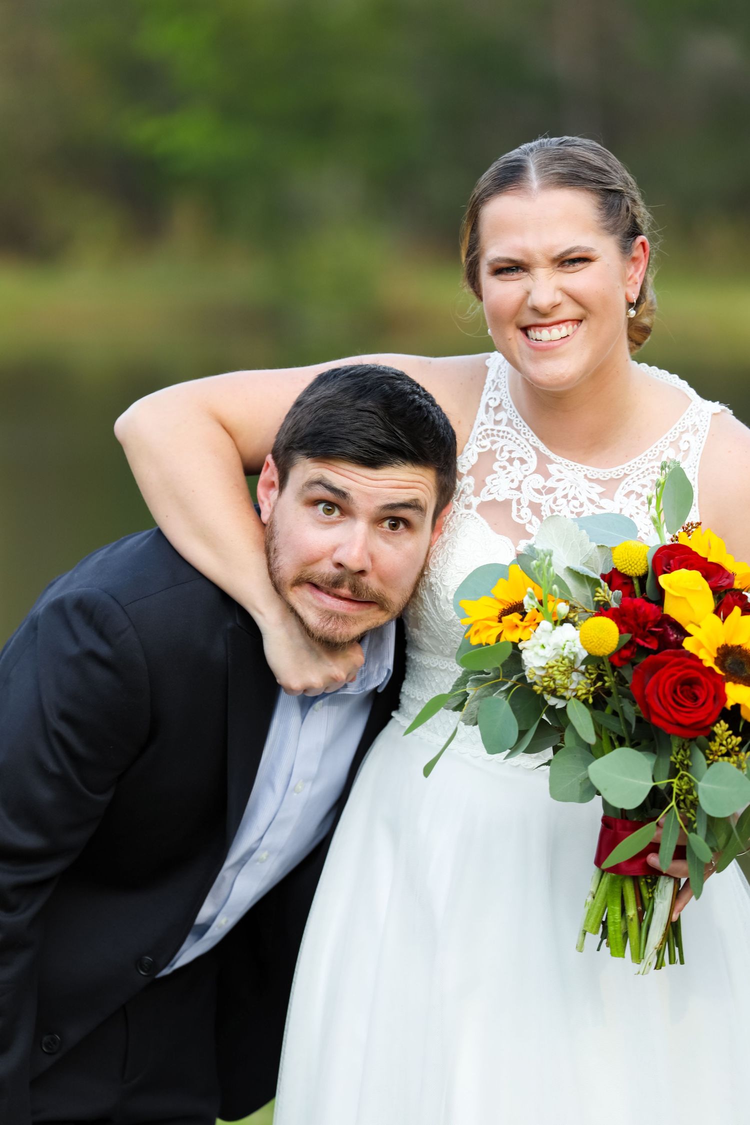 Happy couple poses together with vibrant red and yellow bouquet during wedding portraits.
