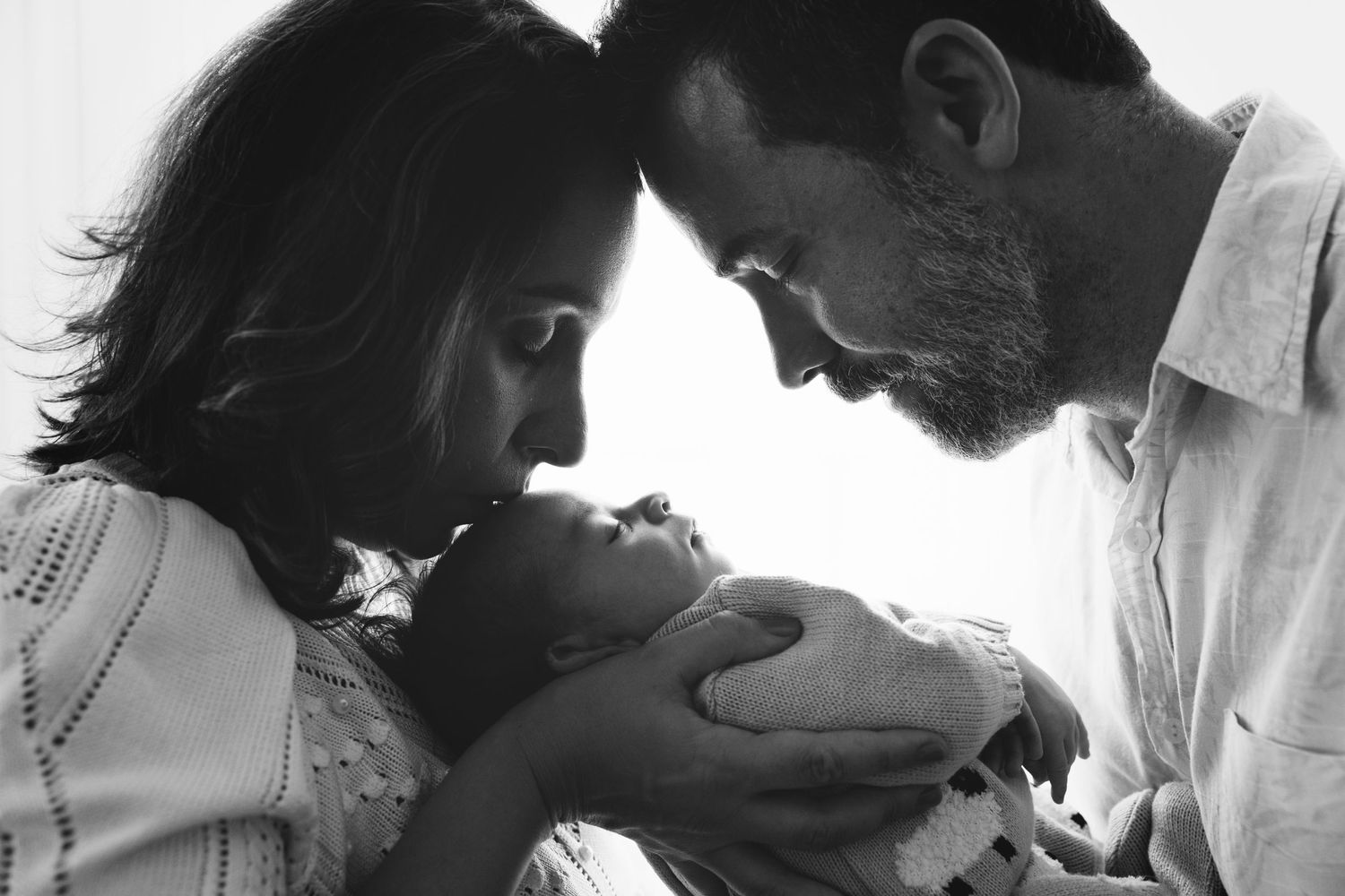 A black and white portrait of parents bonding with their newborn in an intimate setting.