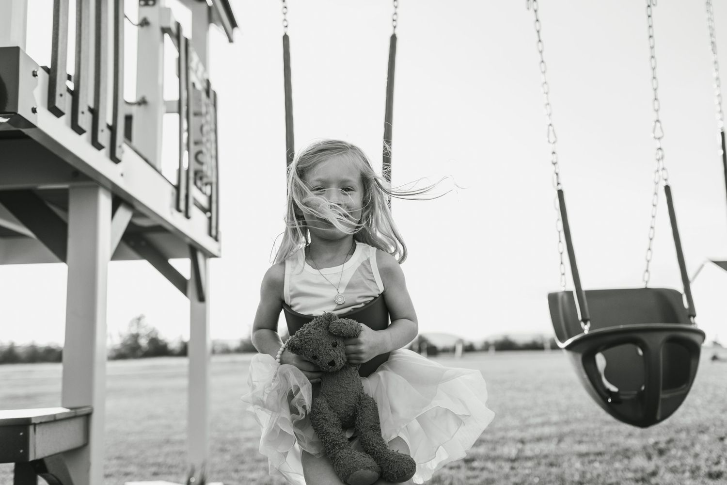 A black and white photo of a child on a playground swing set.