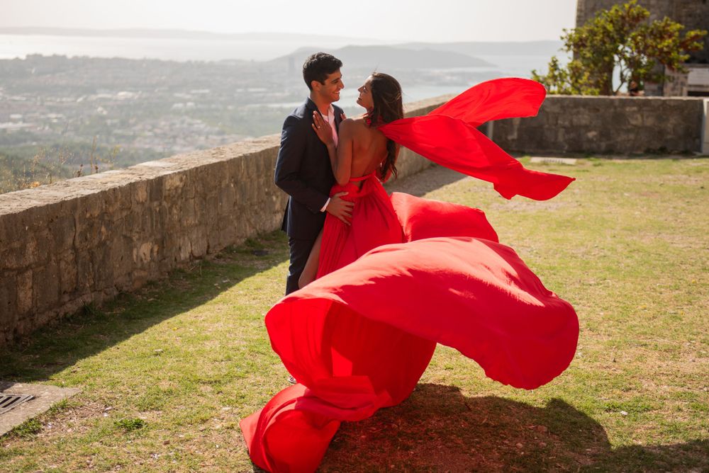 Dramatic red fabric flows around a couple during a romantic photoshoot on a mountain overlook.