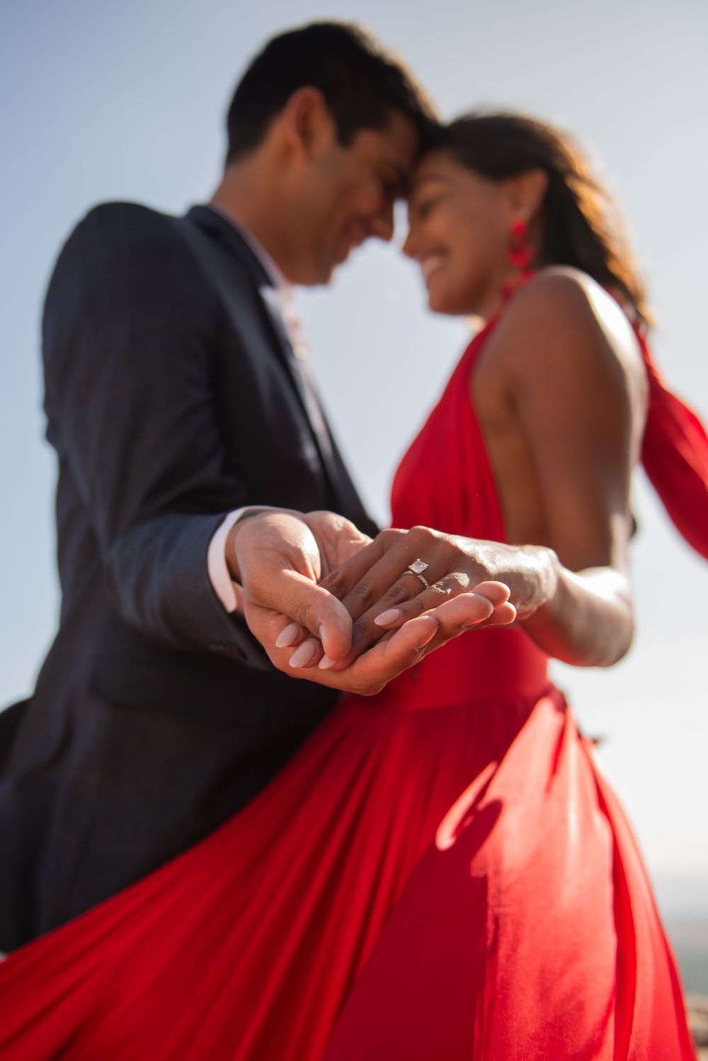 A romantic moment captured with a red flowing dress and ring detail in focus.