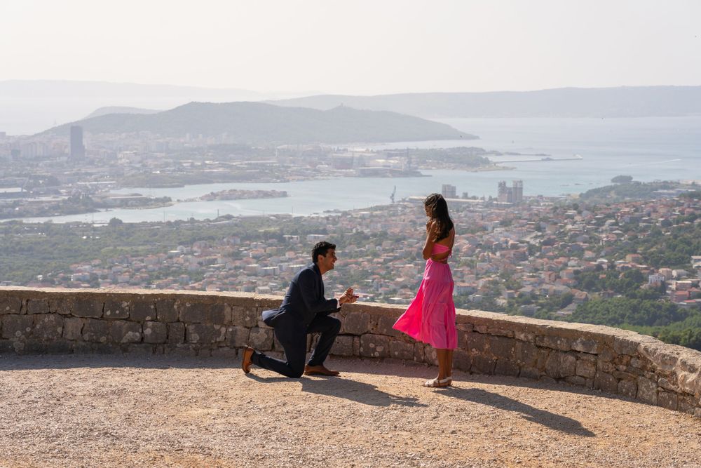 A scenic marriage proposal at a mountain viewpoint overlooking a coastal city.