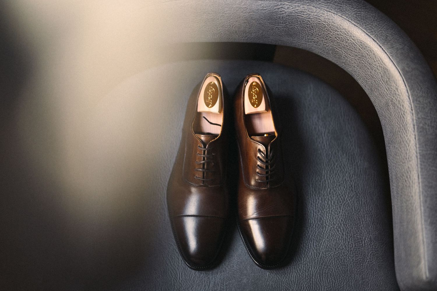 Classic brown leather dress shoes displayed on dark curved surface.