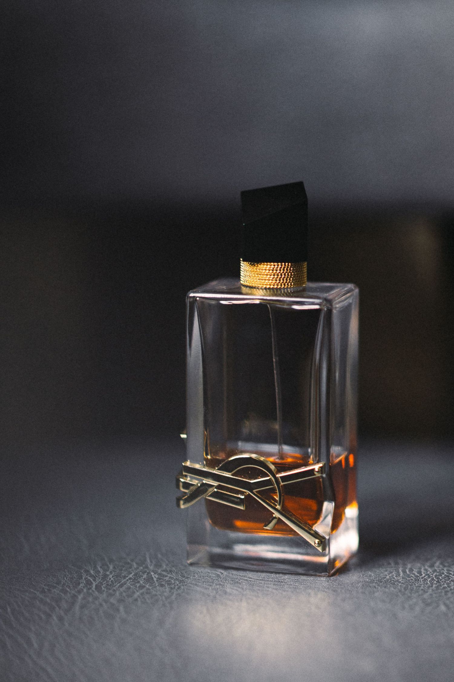 Luxury perfume bottle with amber liquid photographed against dark background.