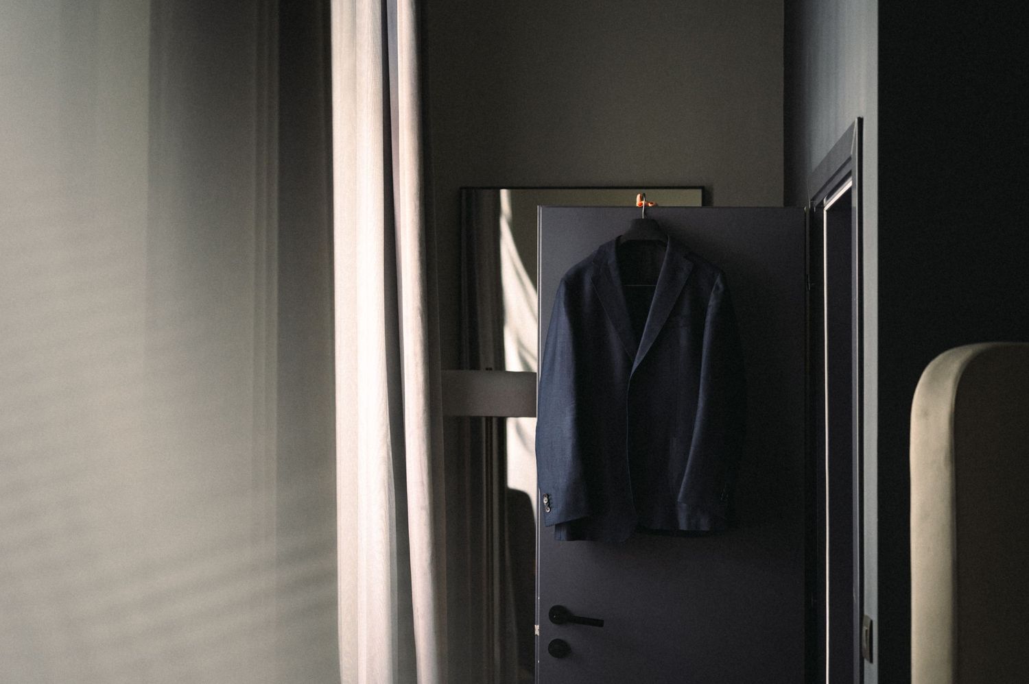 A dark suit jacket hangs on a door in dim lighting creating a moody atmosphere.