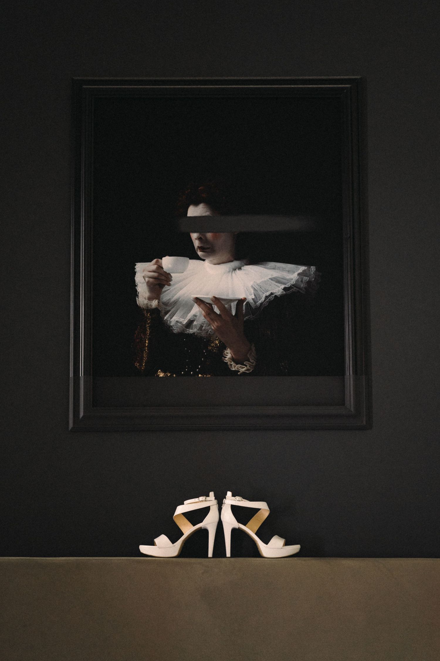 A dramatic black-framed photograph above white wedding shoes against a dark wall.