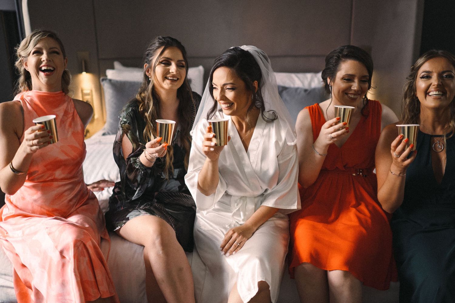 Bridal party in vibrant dresses share drinks and laughs before the ceremony.
