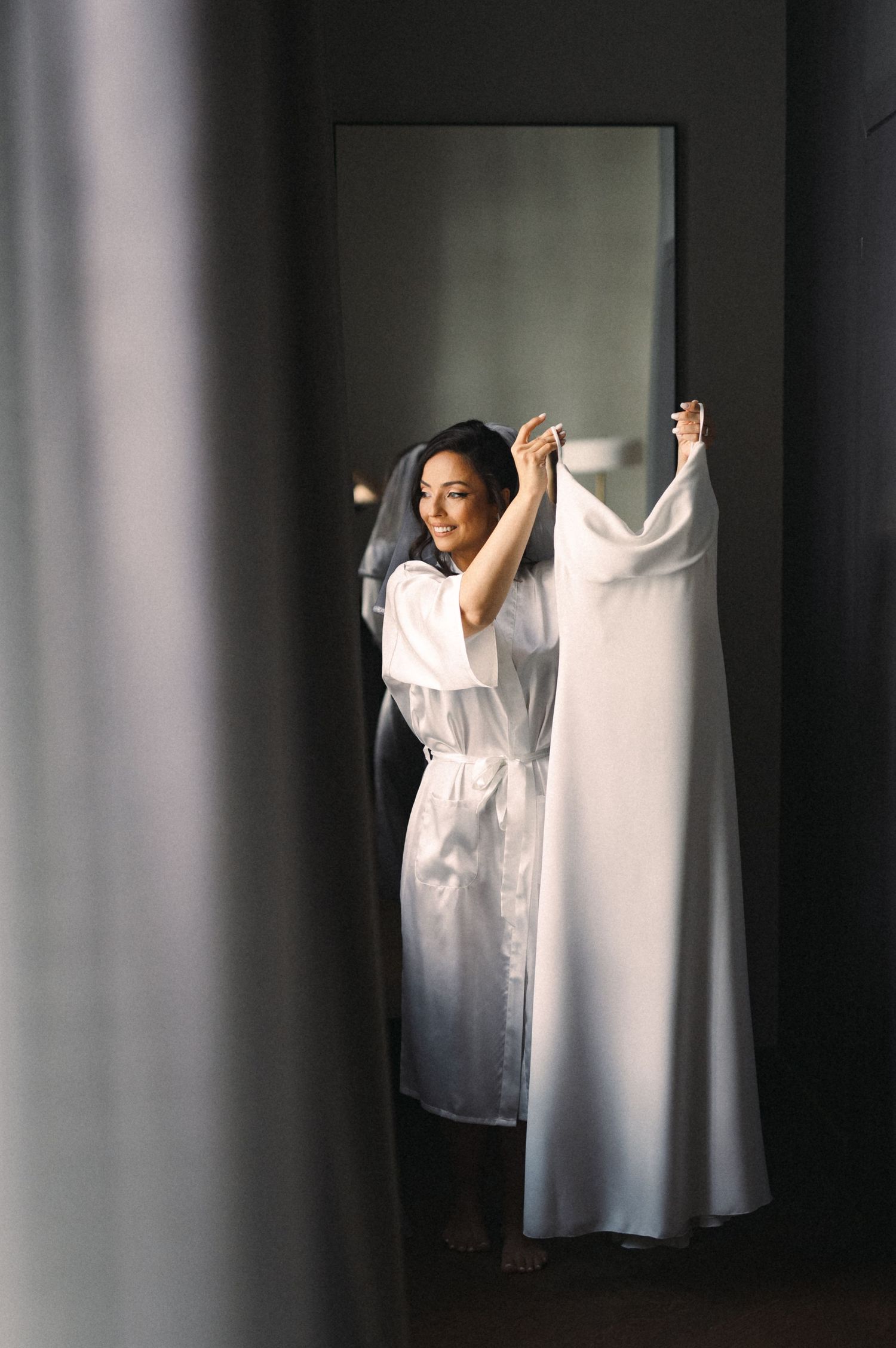 A wedding dress hangs in soft window light as preparations begin.