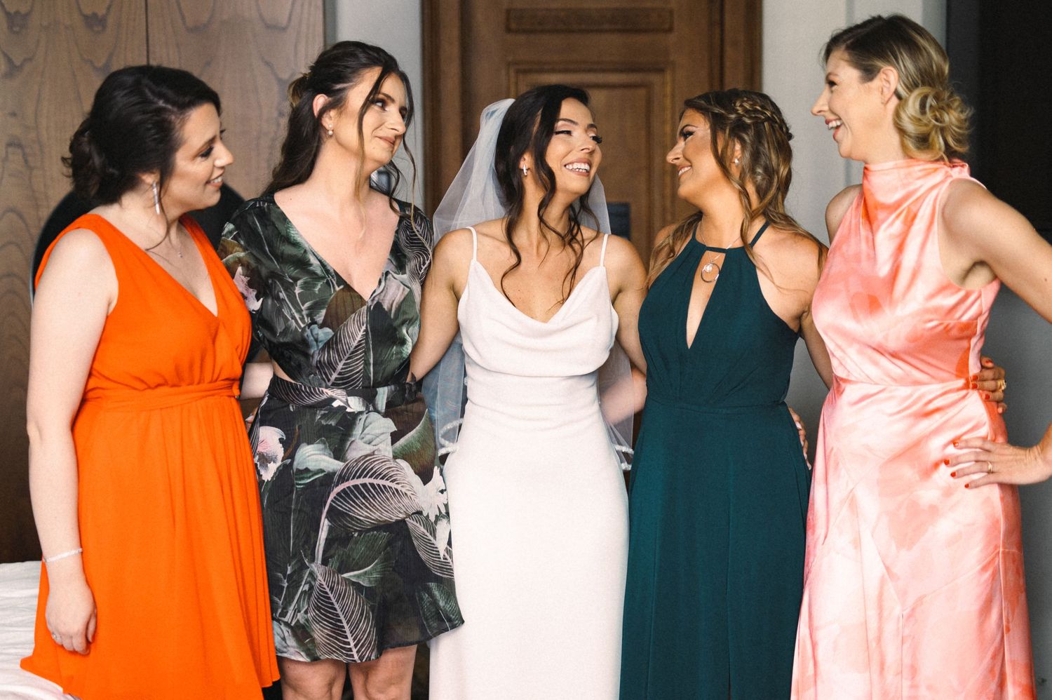 Wedding party in coordinating coral, navy and floral dresses share a joyful moment.