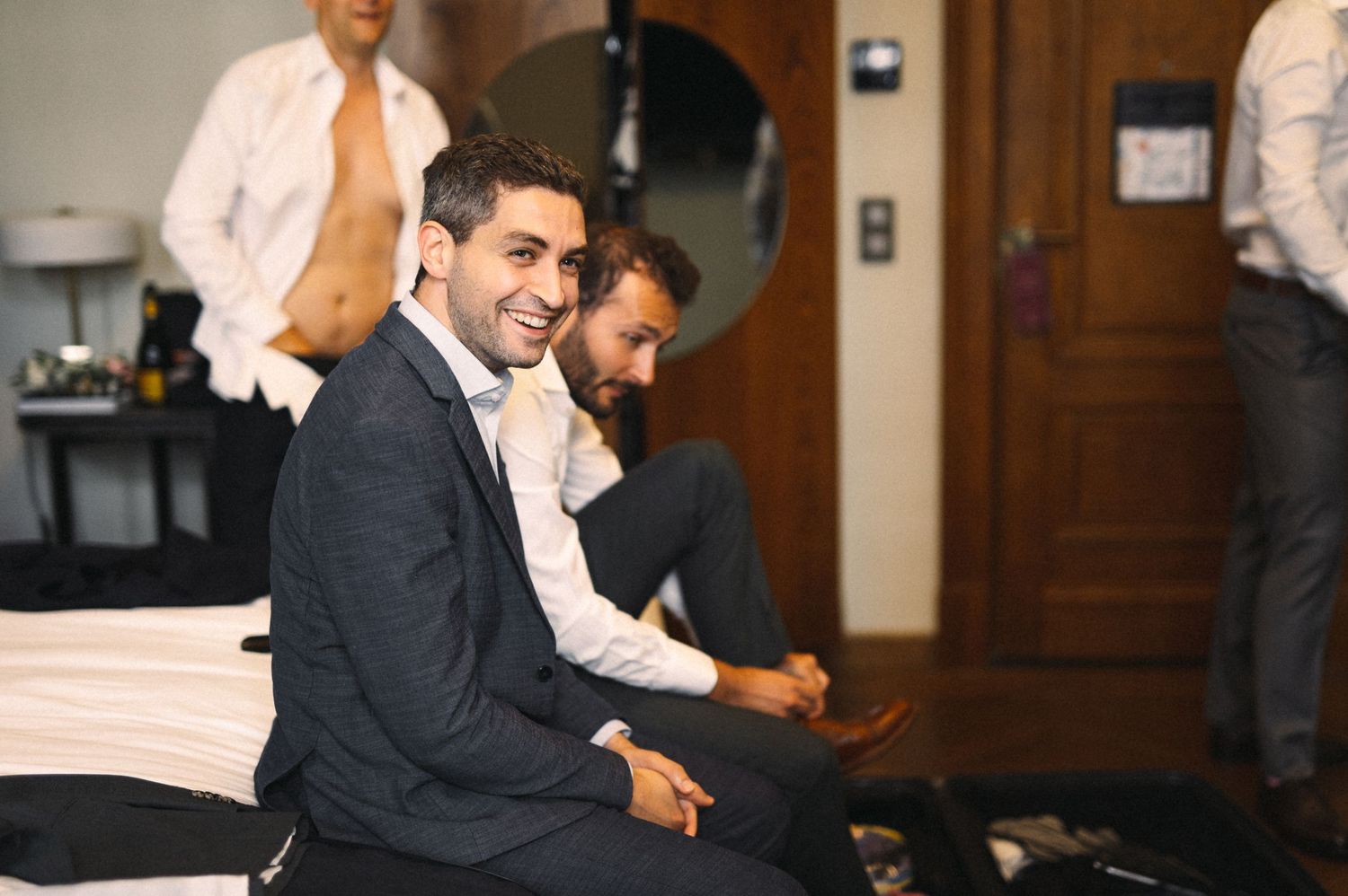 Wedding preparation scene with suited guests in casual conversation.