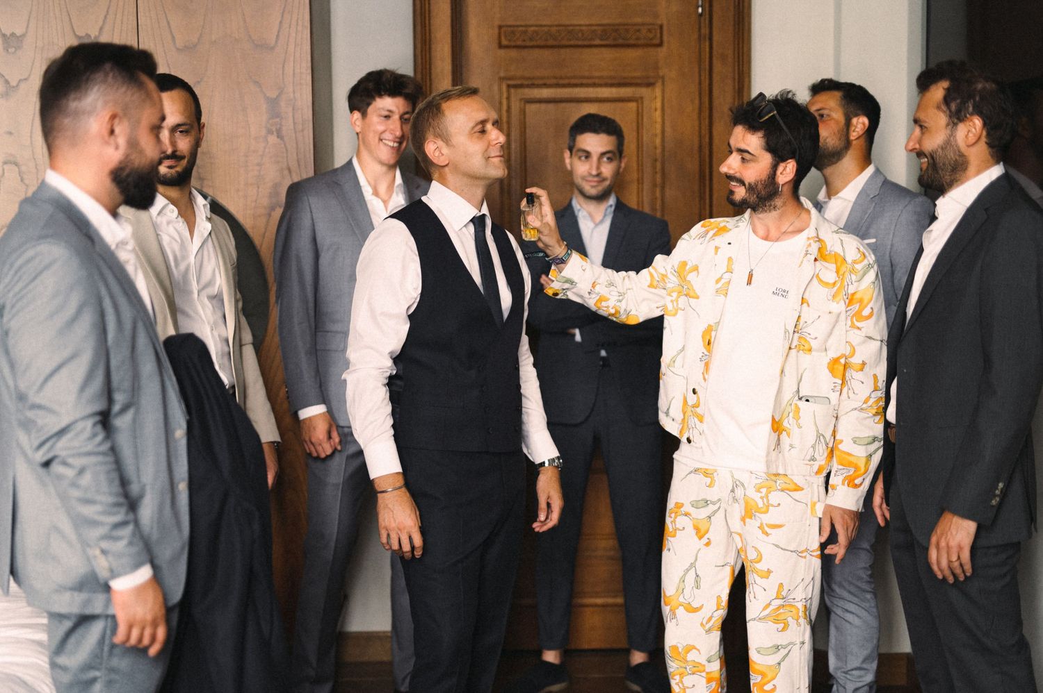 A group of men in suits and one in a patterned outfit gathered in front of a wooden door.
