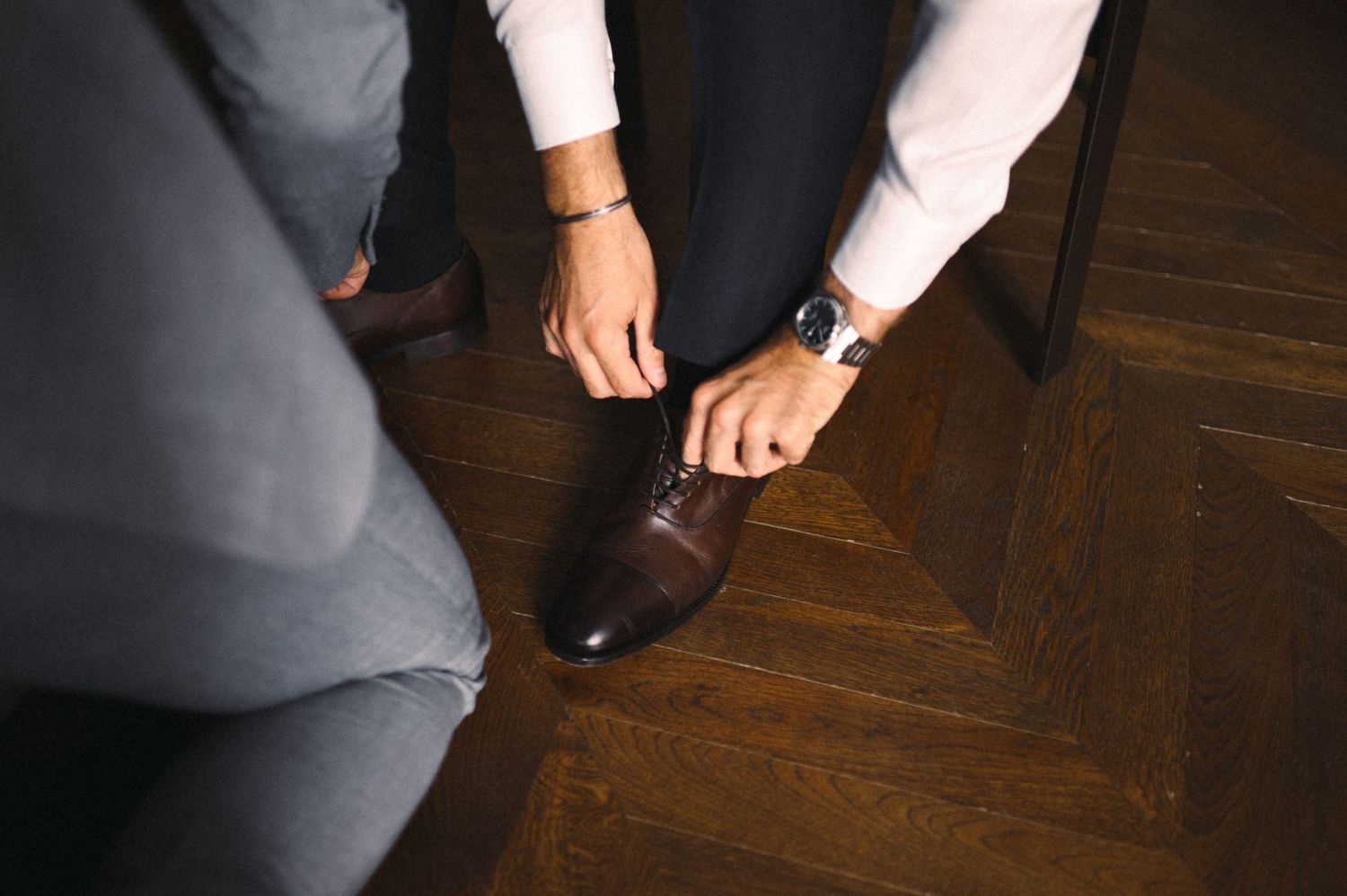 Close-up shot of hands adjusting formal brown leather dress shoes on wooden flooring.