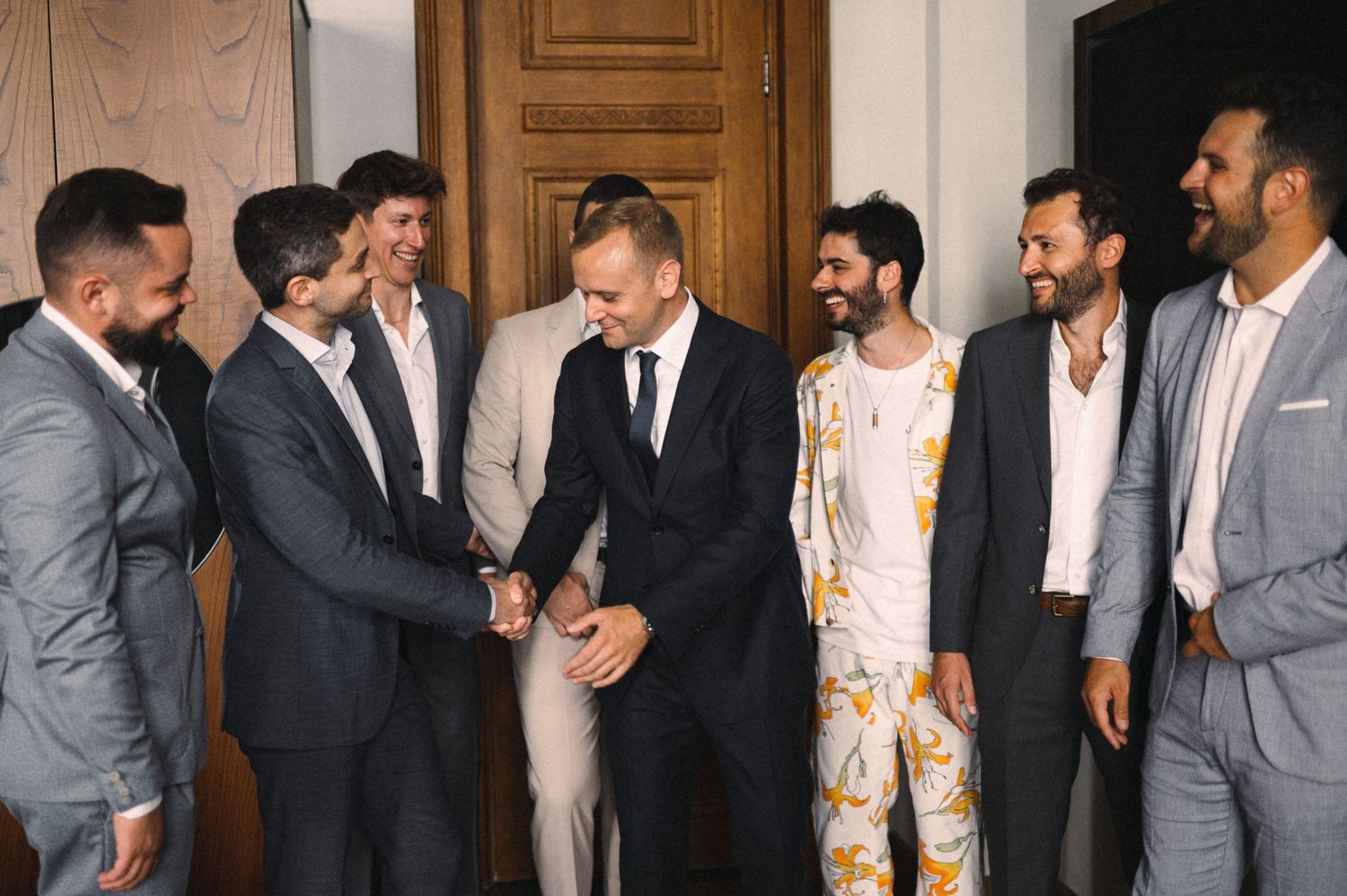 A group of men in suits assisting with formal wear preparations indoors.