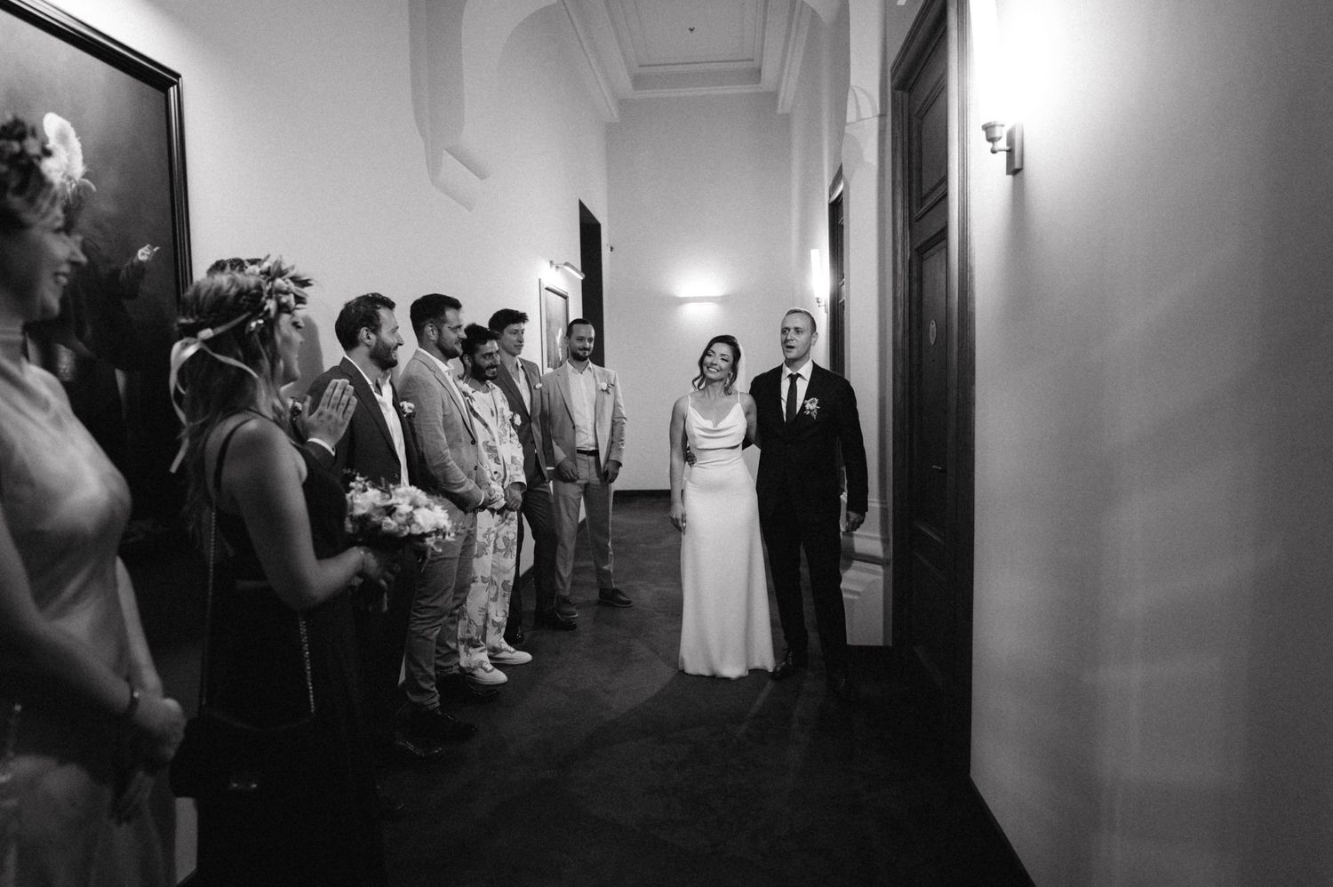 Black and white photo of newlyweds walking down hallway lined with guests.
