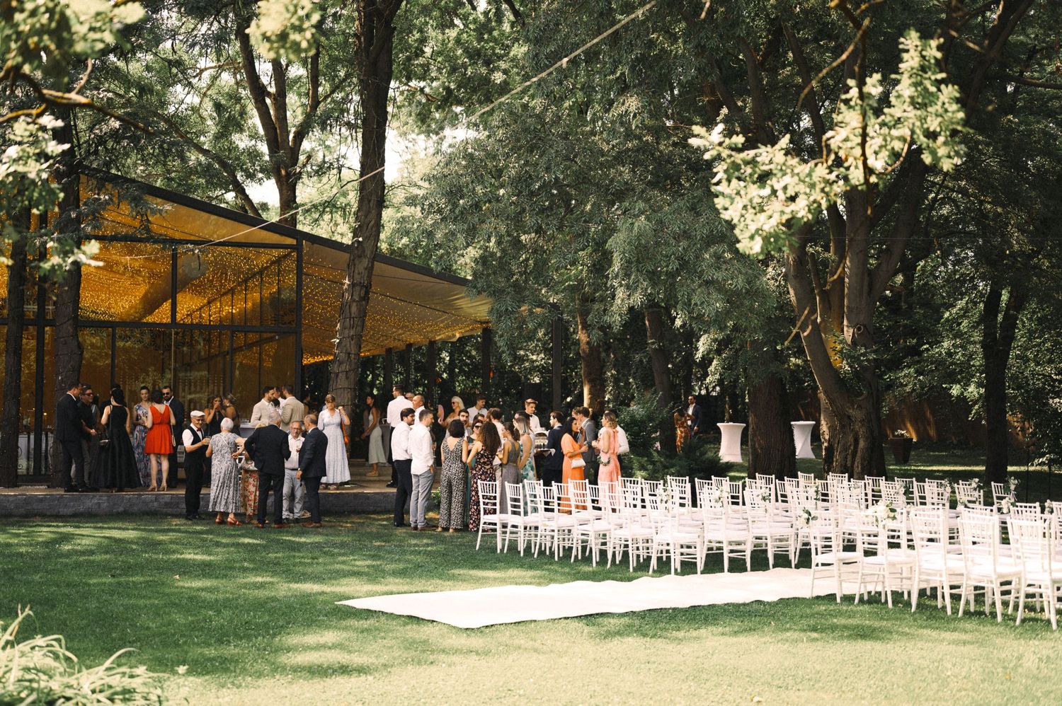 An outdoor wedding ceremony setup with white chairs and a yellow canopy in a wooded setting.