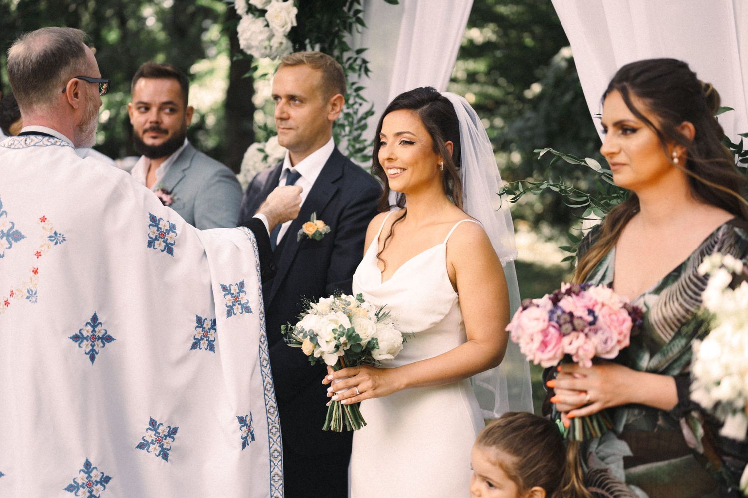 Wedding ceremony with officiant in decorated robe and attendants holding bouquets.