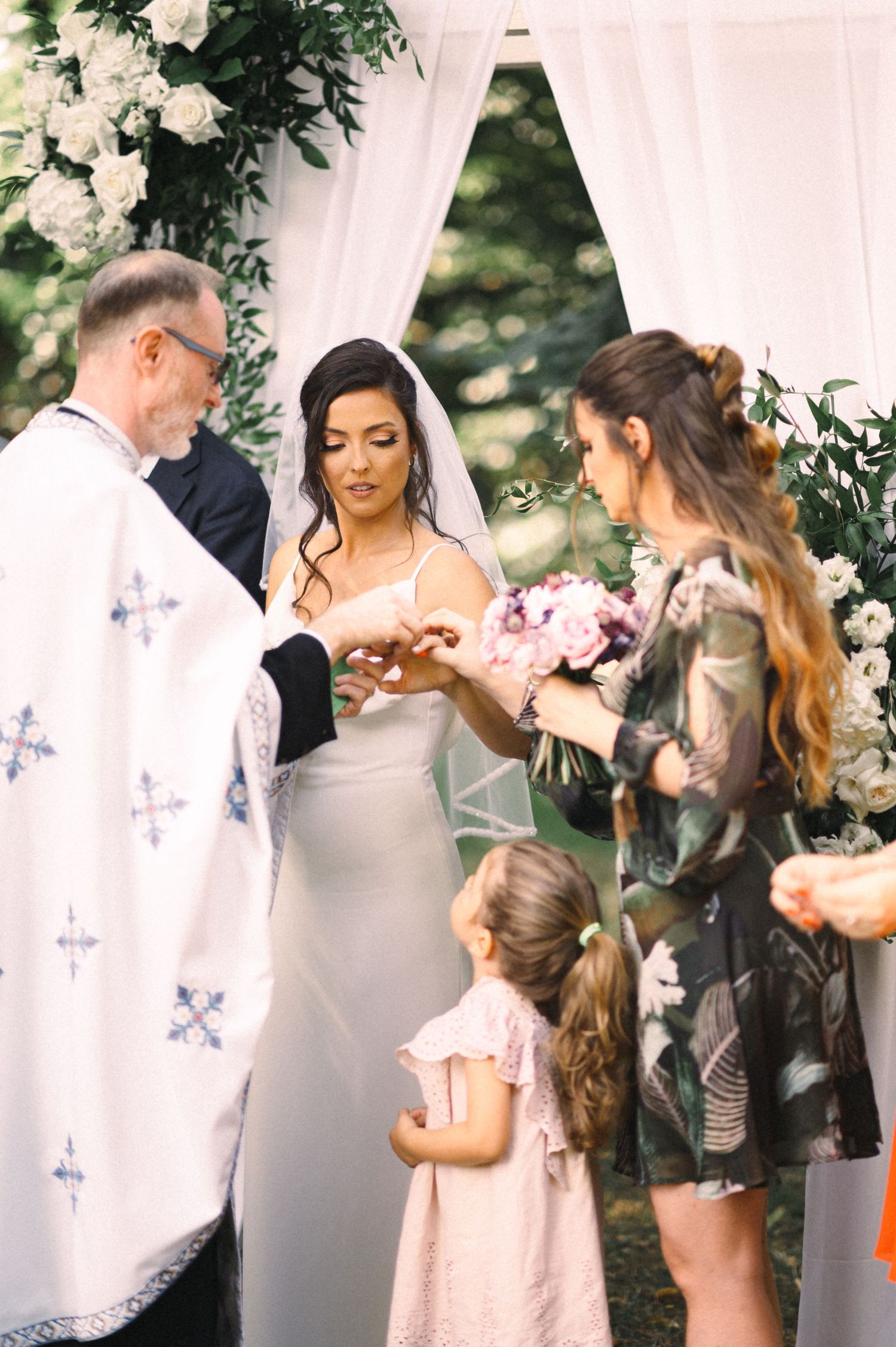 Wedding ring exchange moment during ceremony under floral arch with attendants.